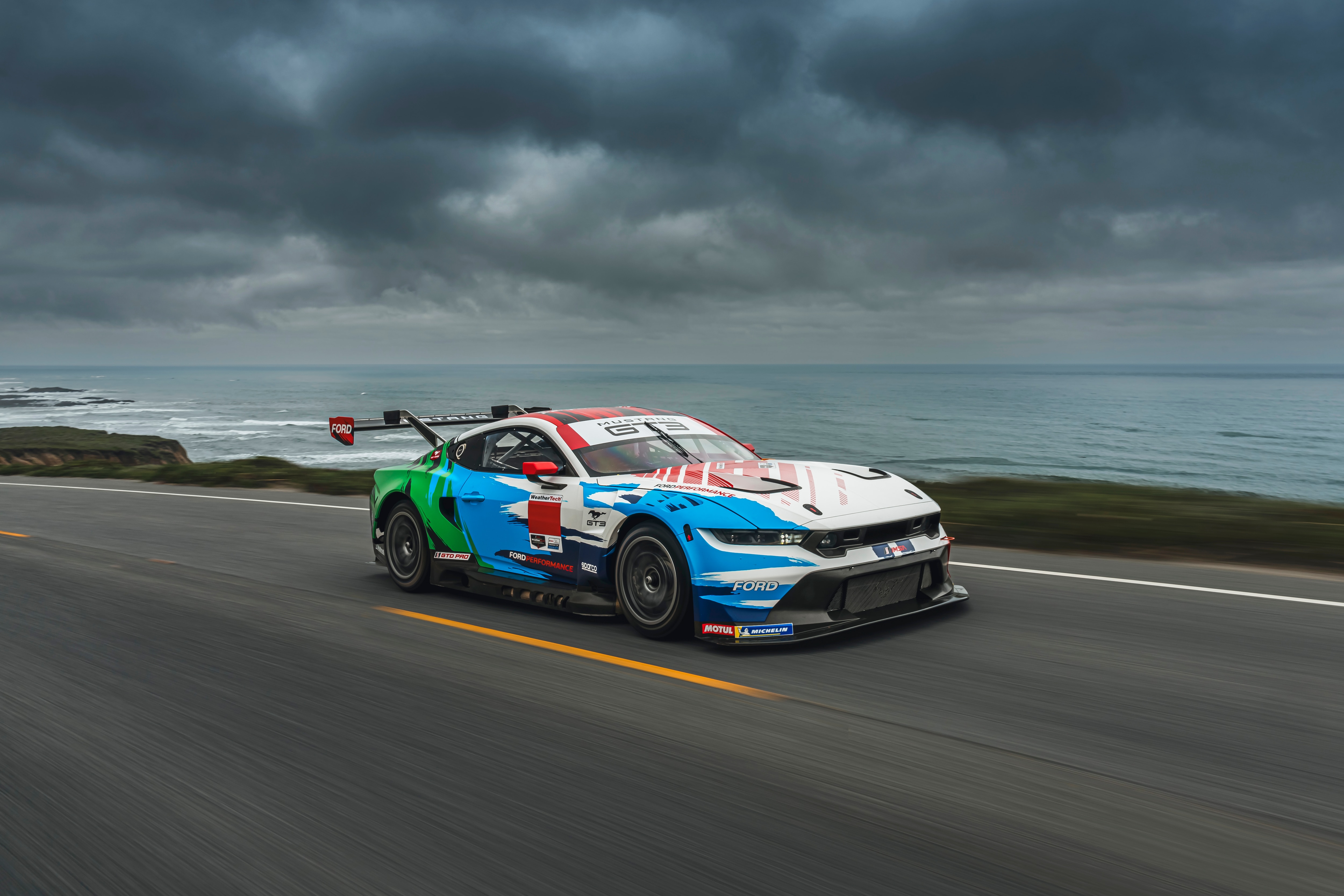 Mustang GT3 in Champion Spirit livery driving on road on the coast of California.