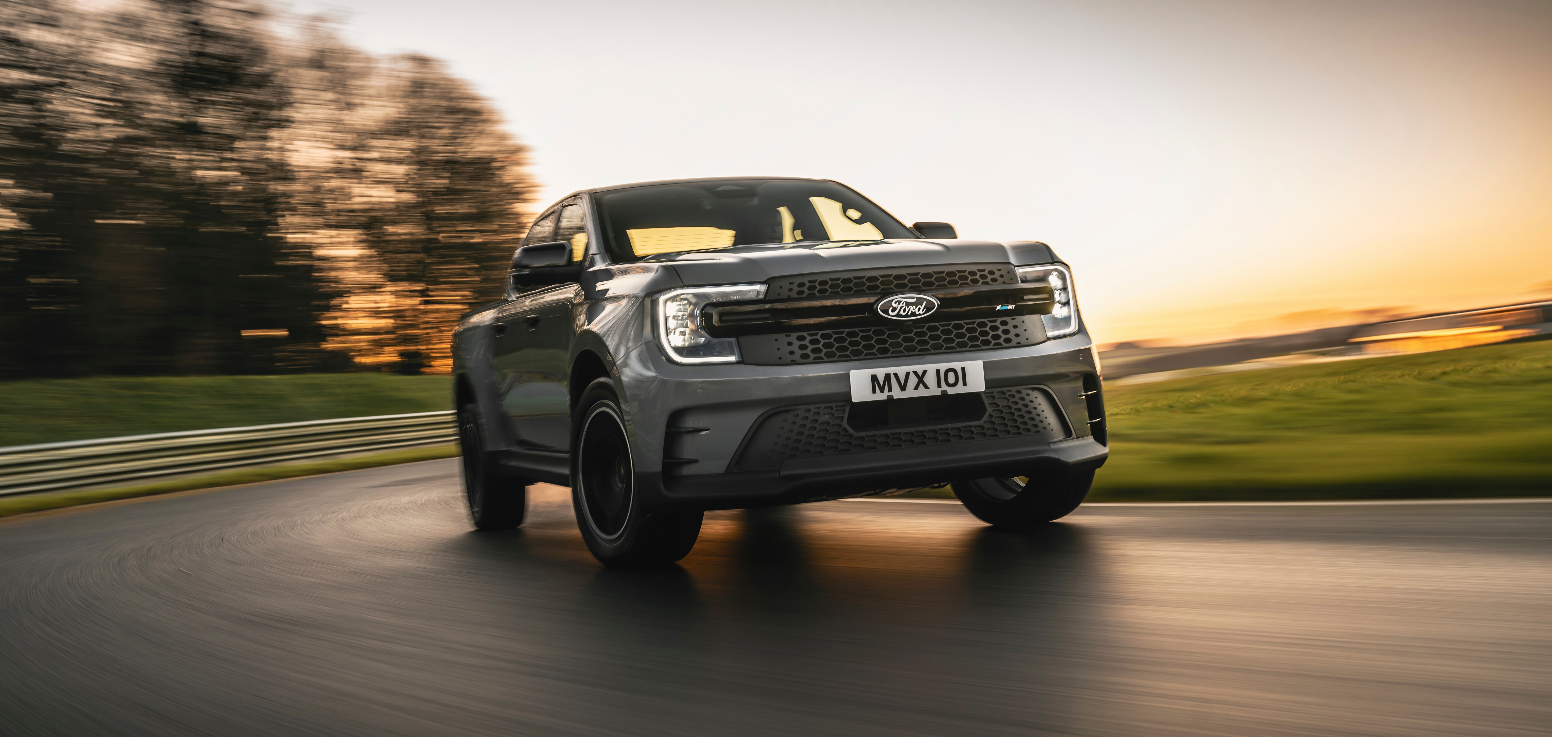 A grey pickup speeding around a racetrack at sunset