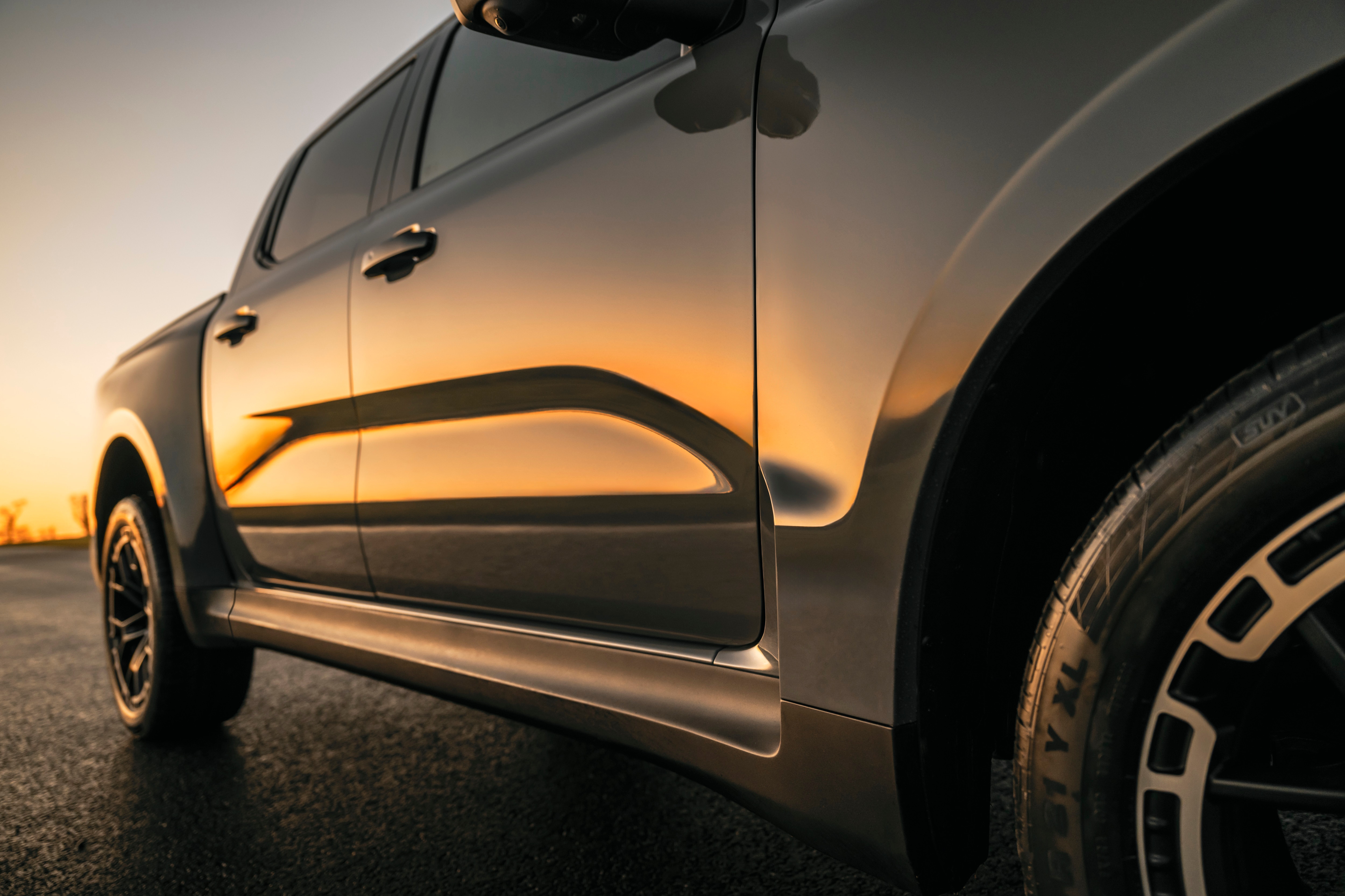 A closeup of a grey pickup reflecting a sunset