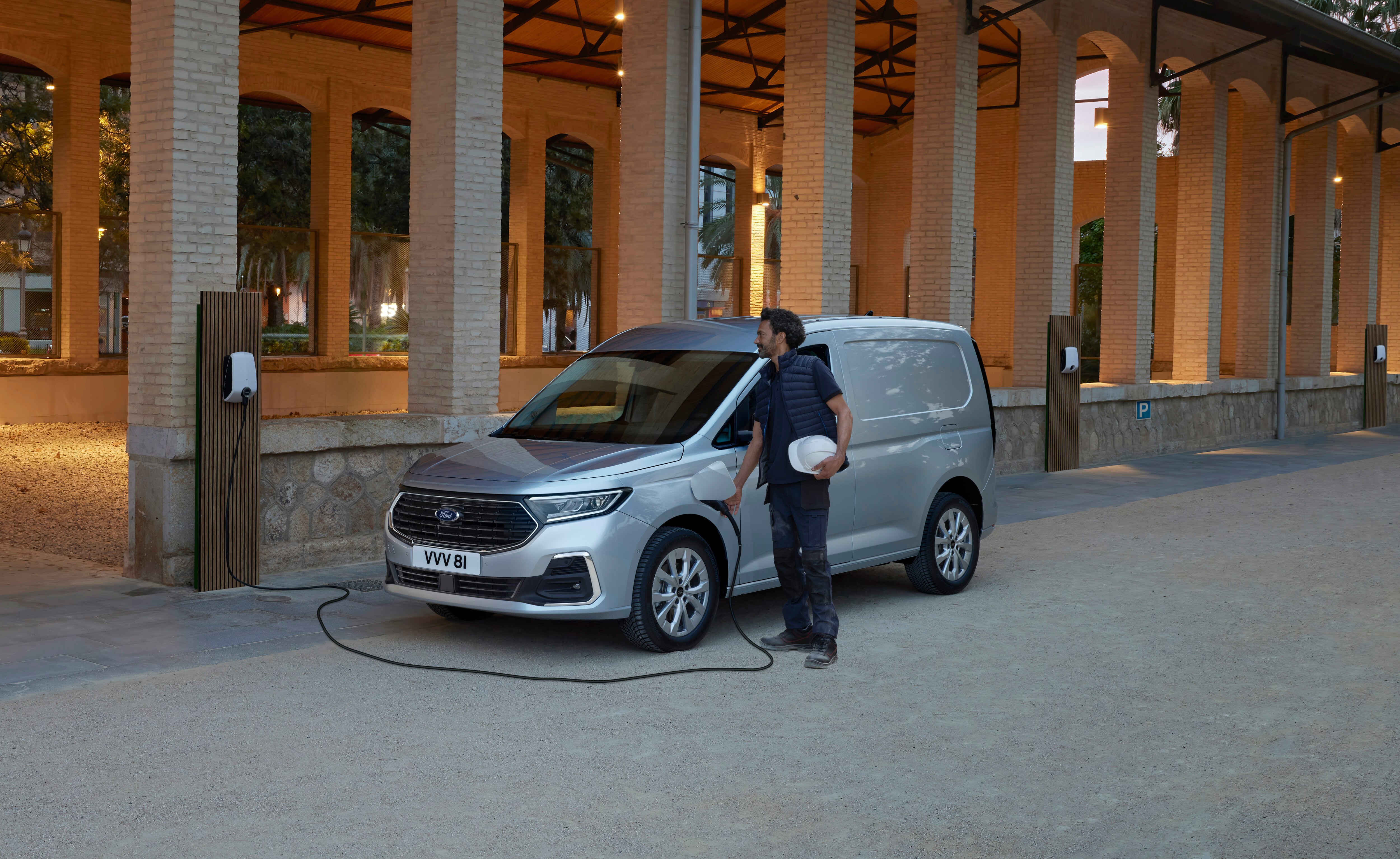an electric van charging by columns with a worker next to it