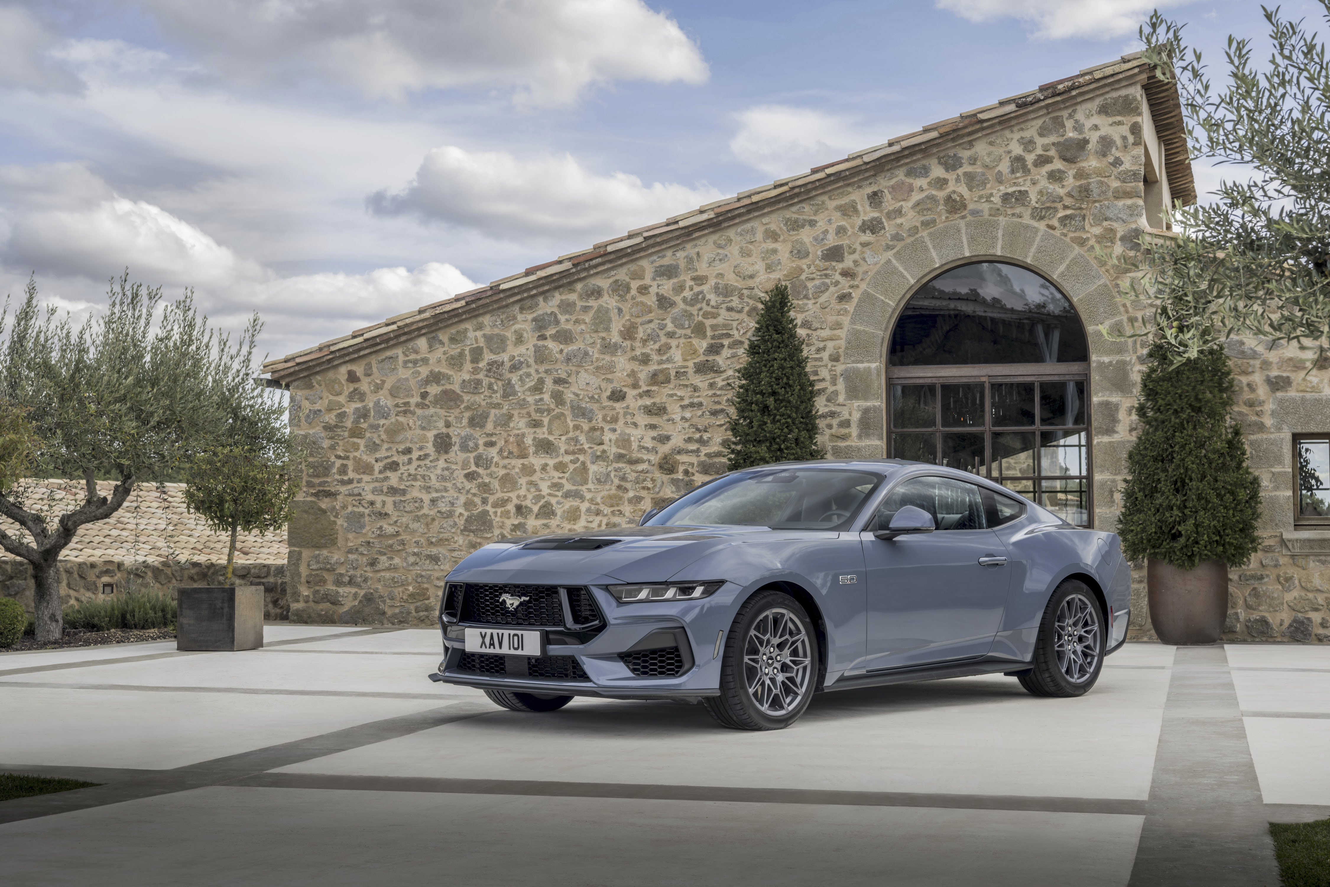 a blue Ford Mustang parked outside a rustic house