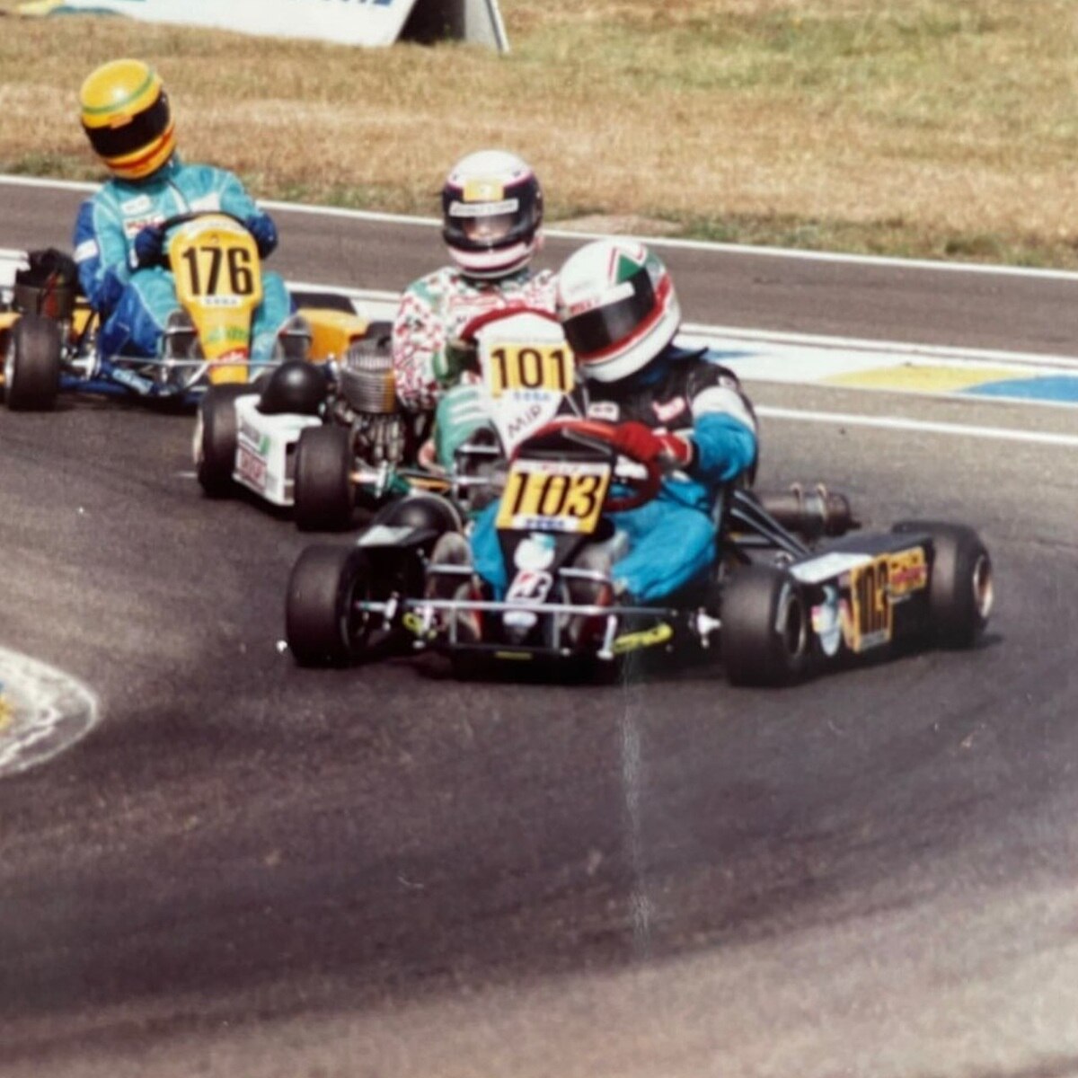 Guy in white, green and red go kart chasing leader through a fast corner with motion blur on the photo