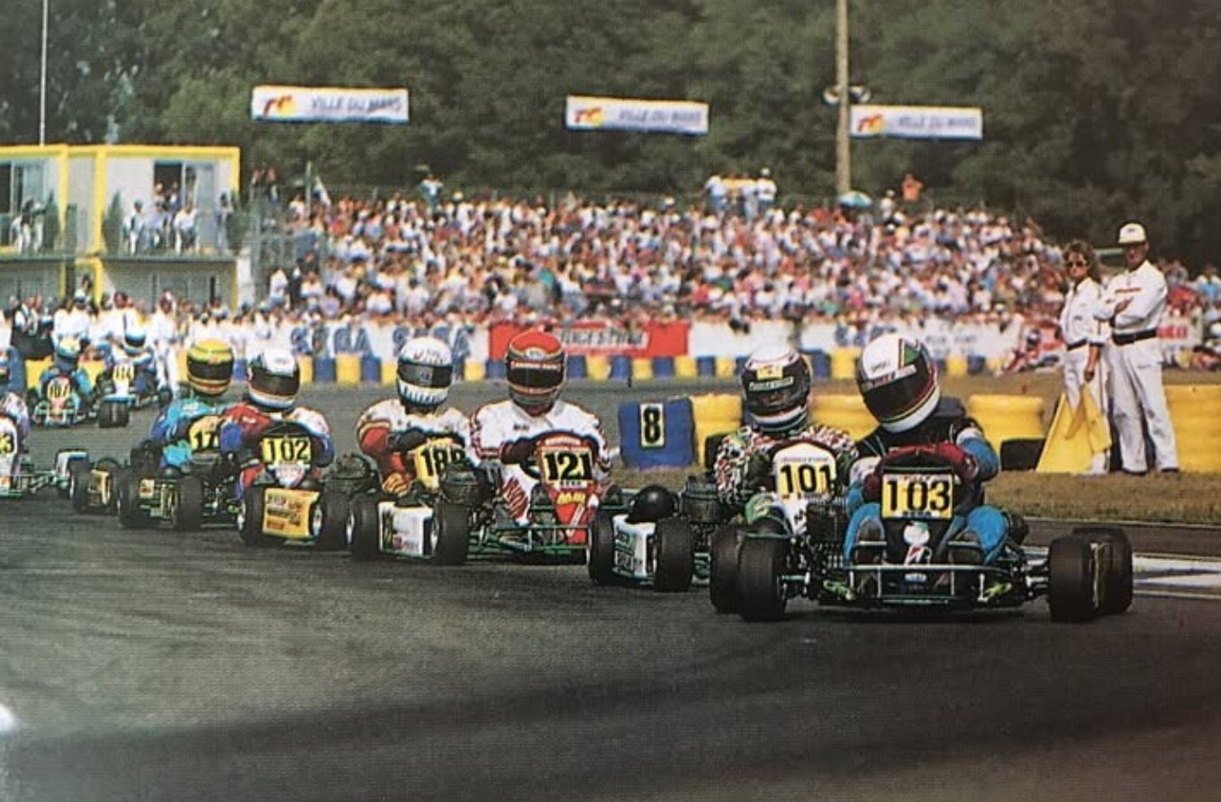 Brightly coloured karts and big crowd in the background watching Guy racing in the 1990s