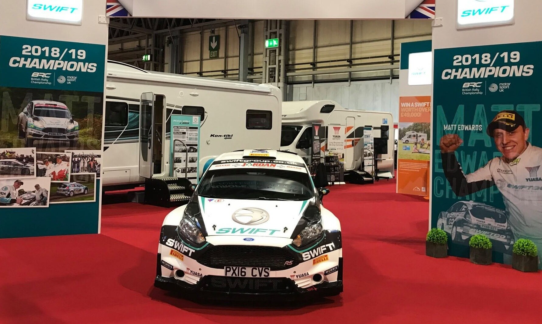 Ford Fiesta rally car in Swift livery parked on the company stand between motorhomes at an indoor motor show