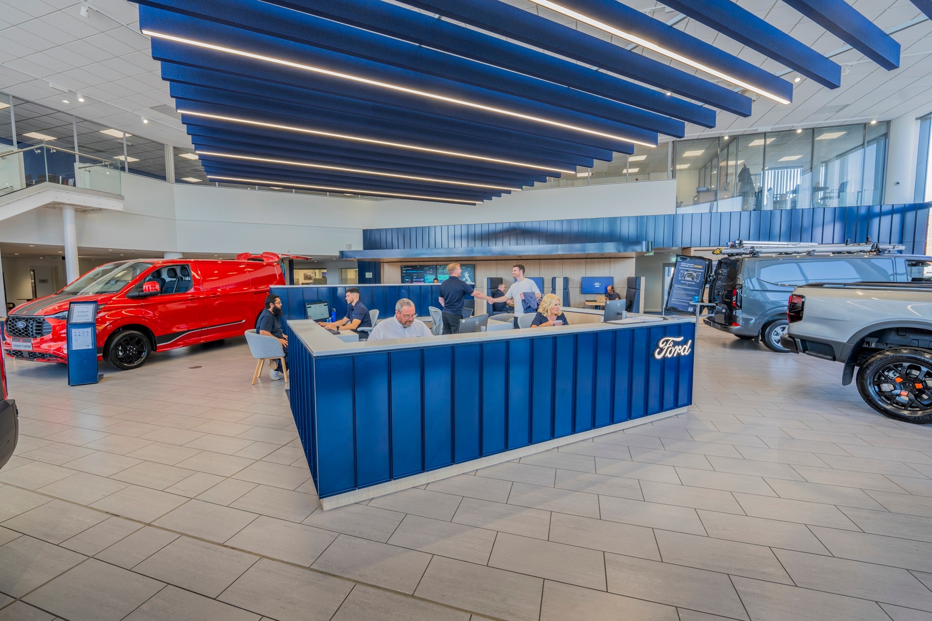 Ford Transit Centre reception with staff in foreground, red Transit Custom on the left and silver Ranger pick-up truck on the right