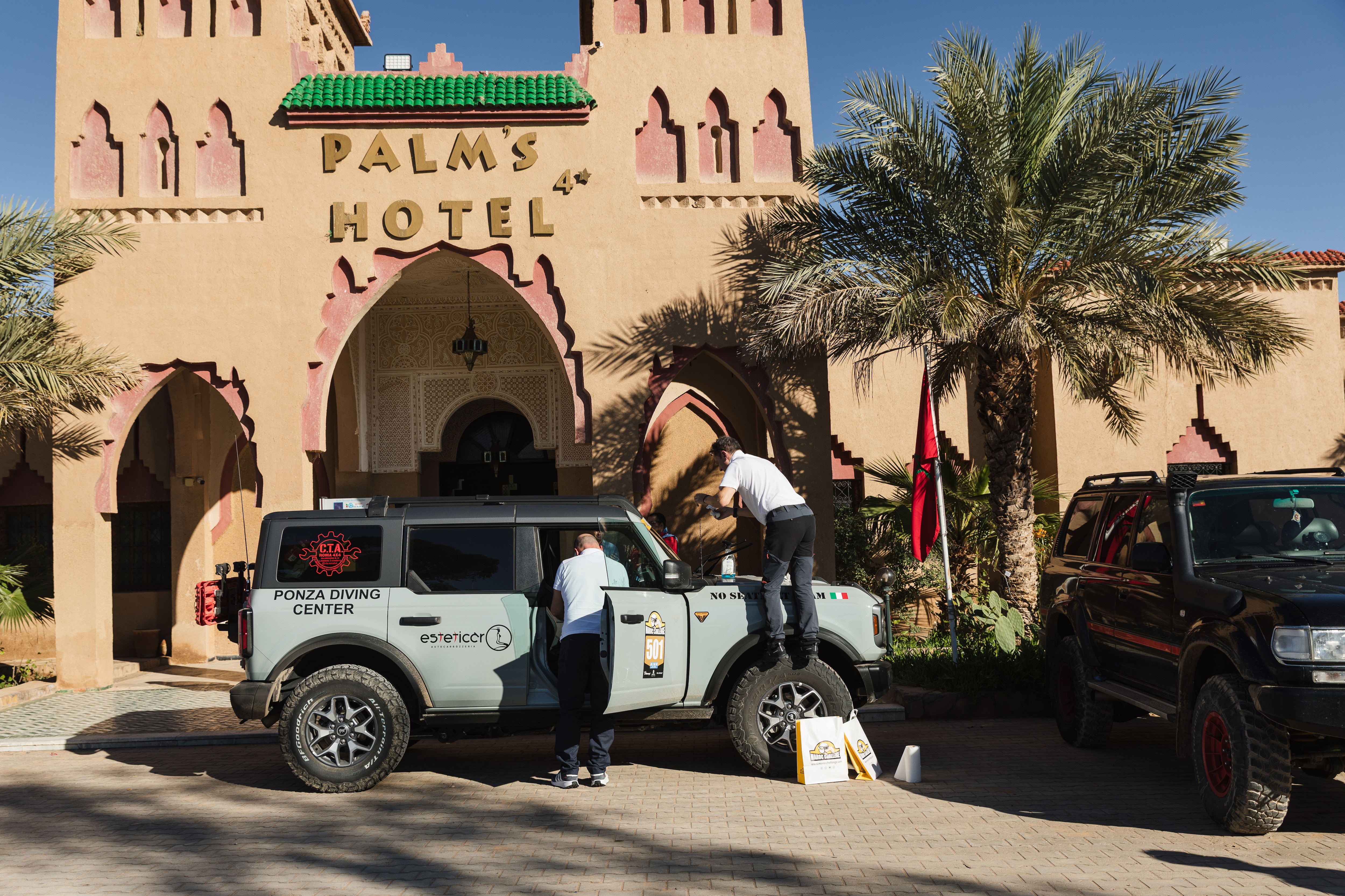 Ford Bronco parked under palm tree outside desert hotel
