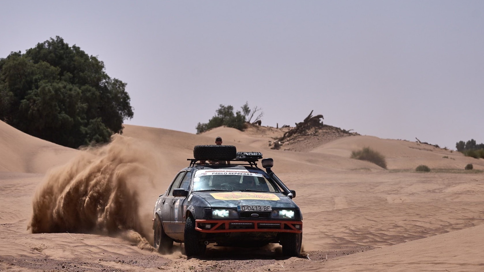 1990s Ford Sierra drifting through the desert with spare tyres on the roof