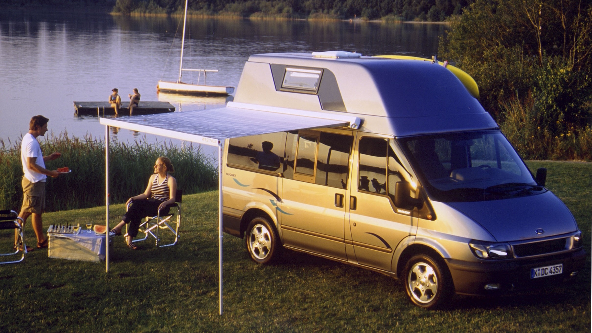 2000 Nugget parked by a lake at sunset while a couple enjoy drinks under the awning
