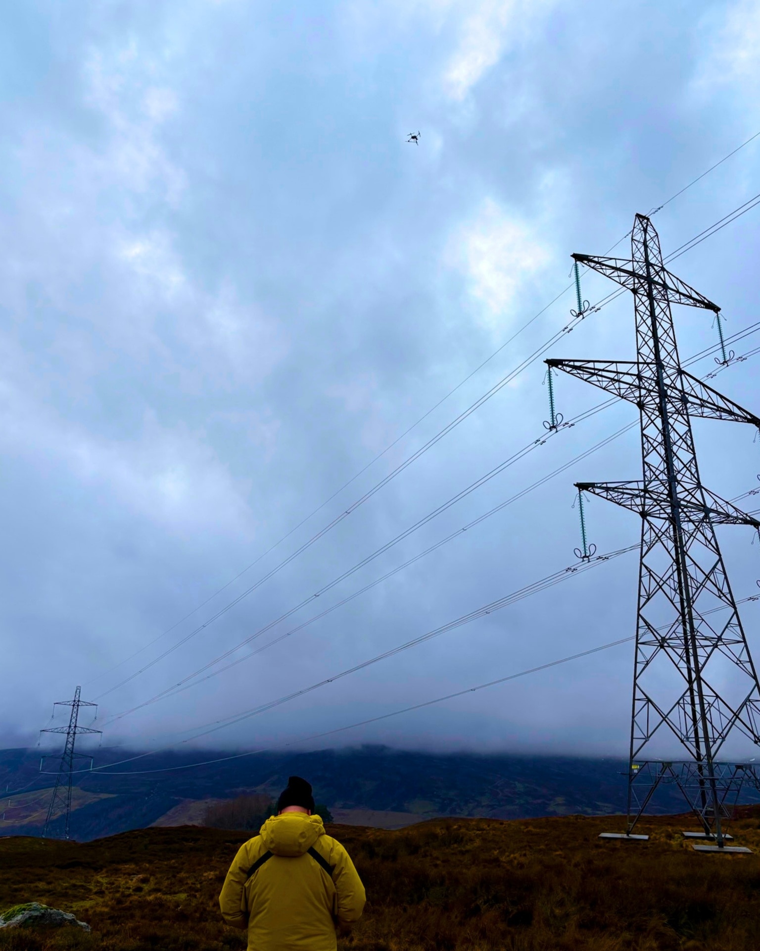 Team UAV drone pilot in high visibility jacket uses a drone to inspect a power line under dark grey skies