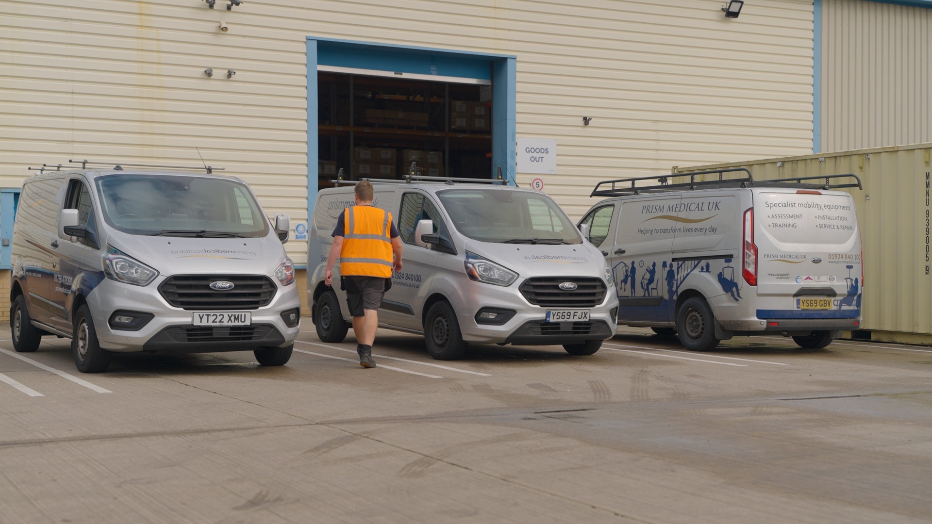Three Prism vans parked in depot with worker in hi-viz jacket walking through door