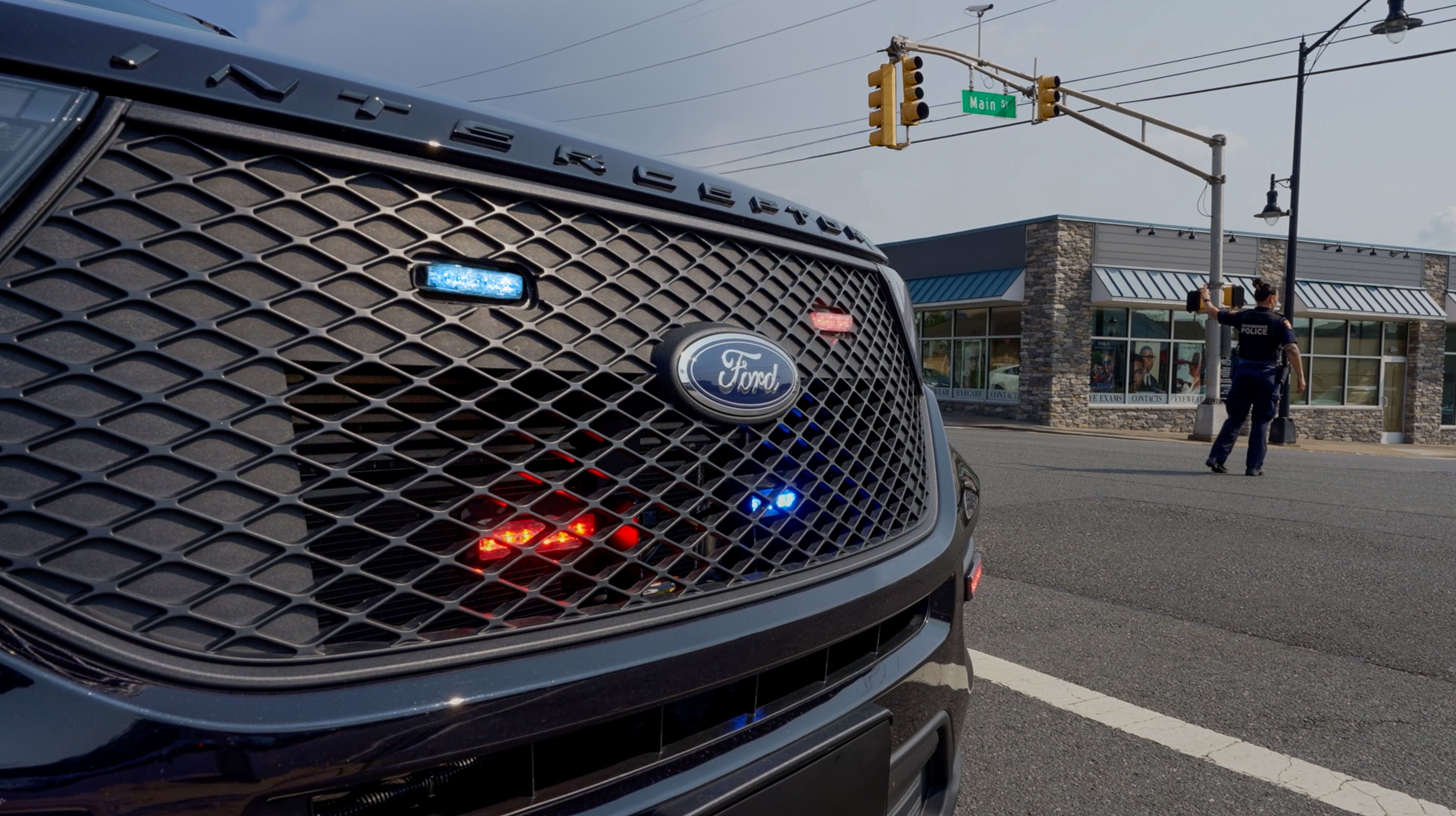 An officer directs traffic with a Ford police vehicle in the foreground.