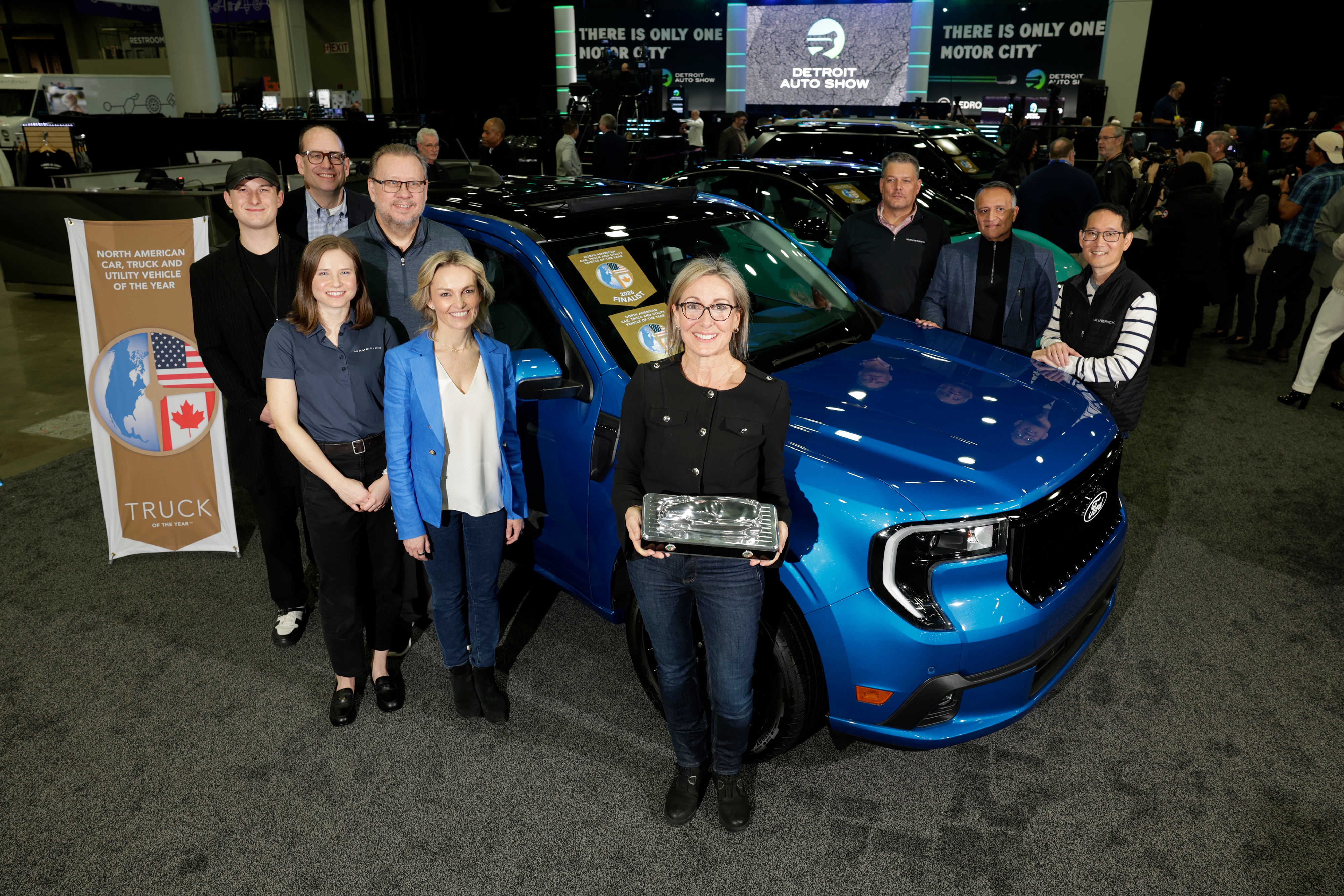 A group of people pose with an award in front of a blue Ford Maverick Lobo.