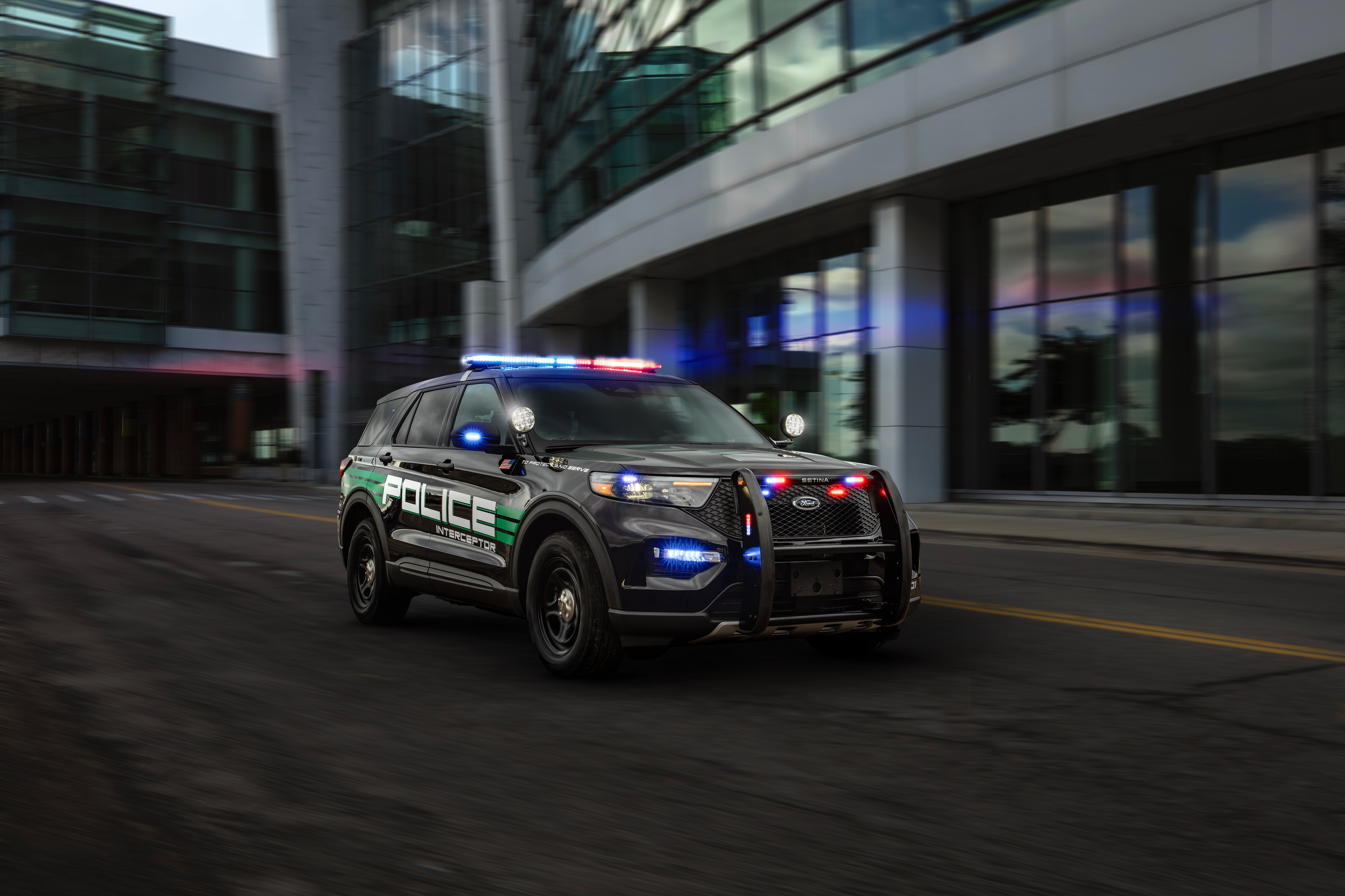 A 2025 Ford Police Interceptor Utility Hybrid driving down a road with the lights on. 