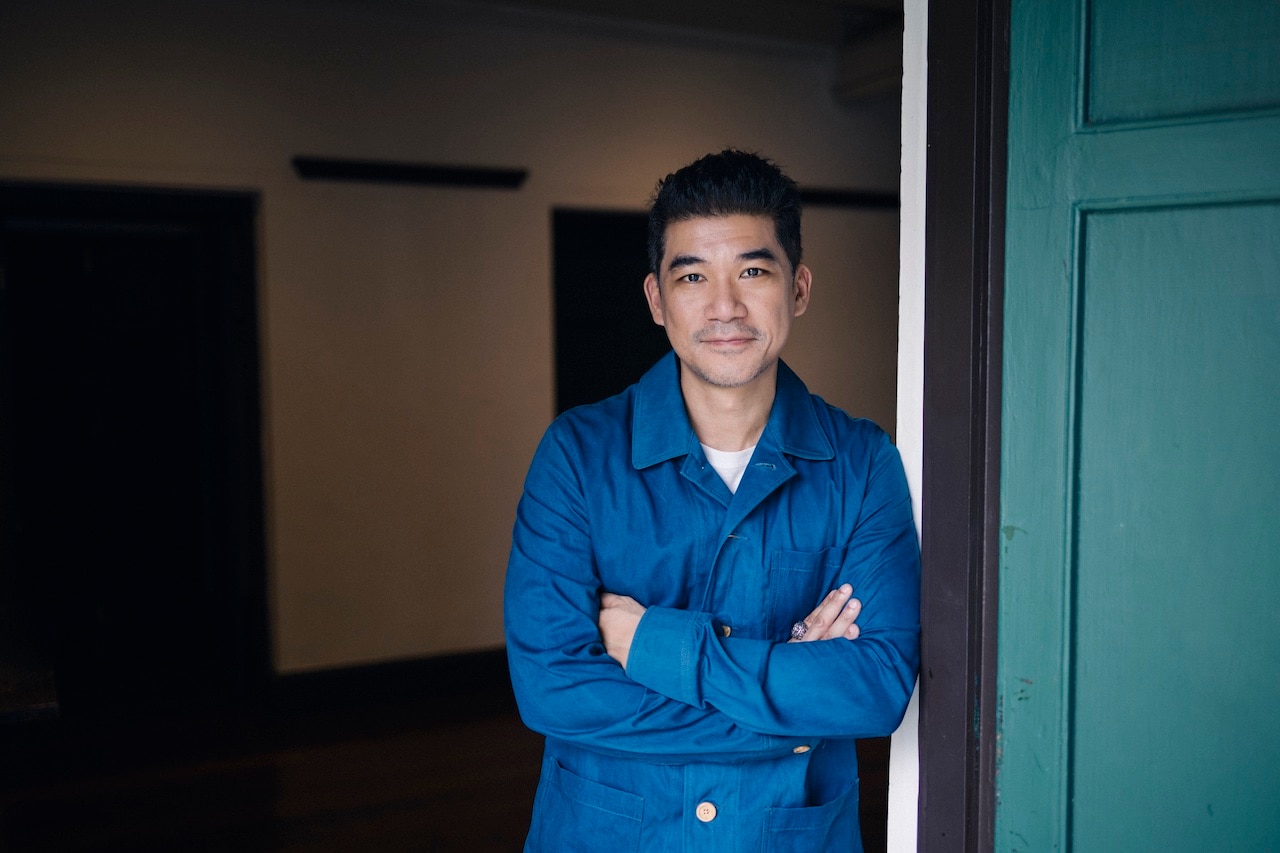 A man in a blue button up shirt crosses his arms and smiles for a photo.