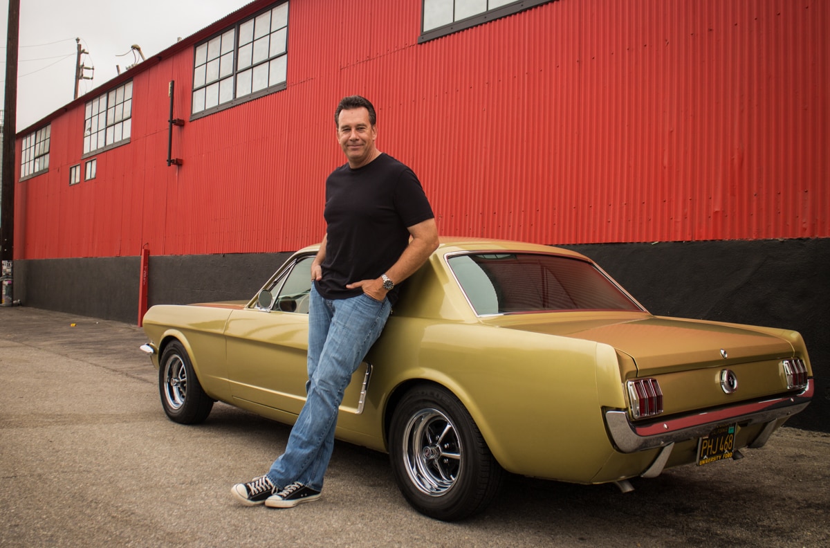 A man leans against a 1960s Mustang.