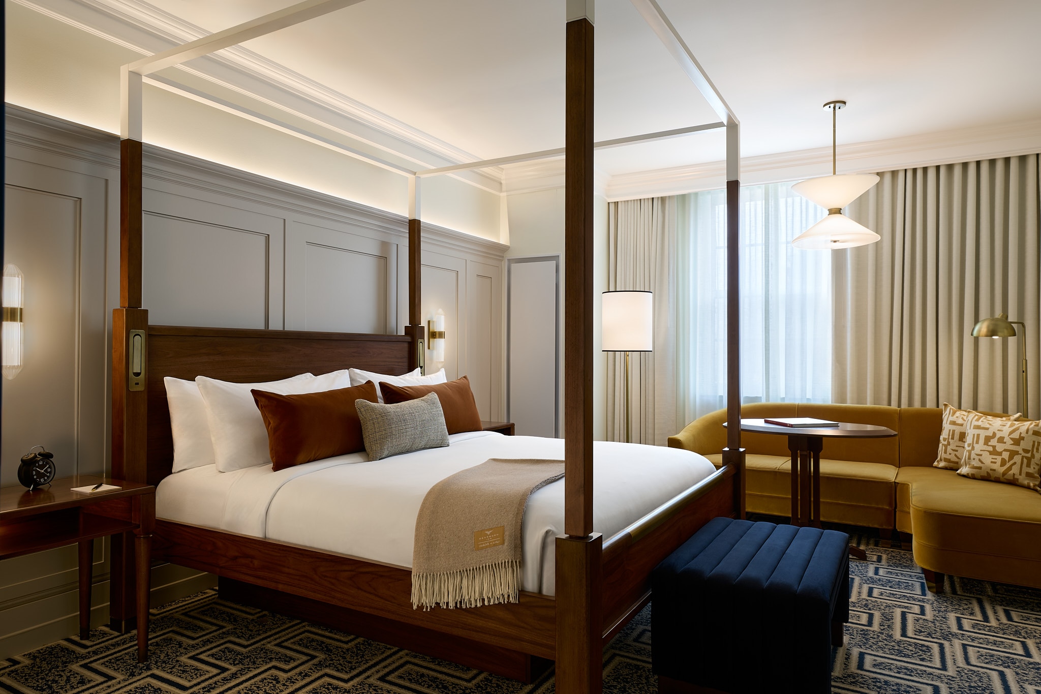 A King Standard room at the newly renovated Dearborn Inn shows corner seating with a small table next to a king-sized bed with white bedding