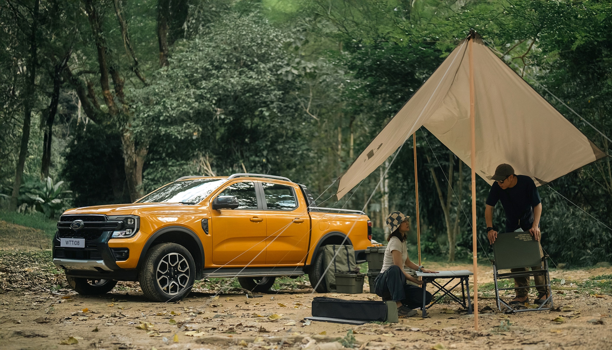 Two people gather near their Ford truck under a tarp in the woods.