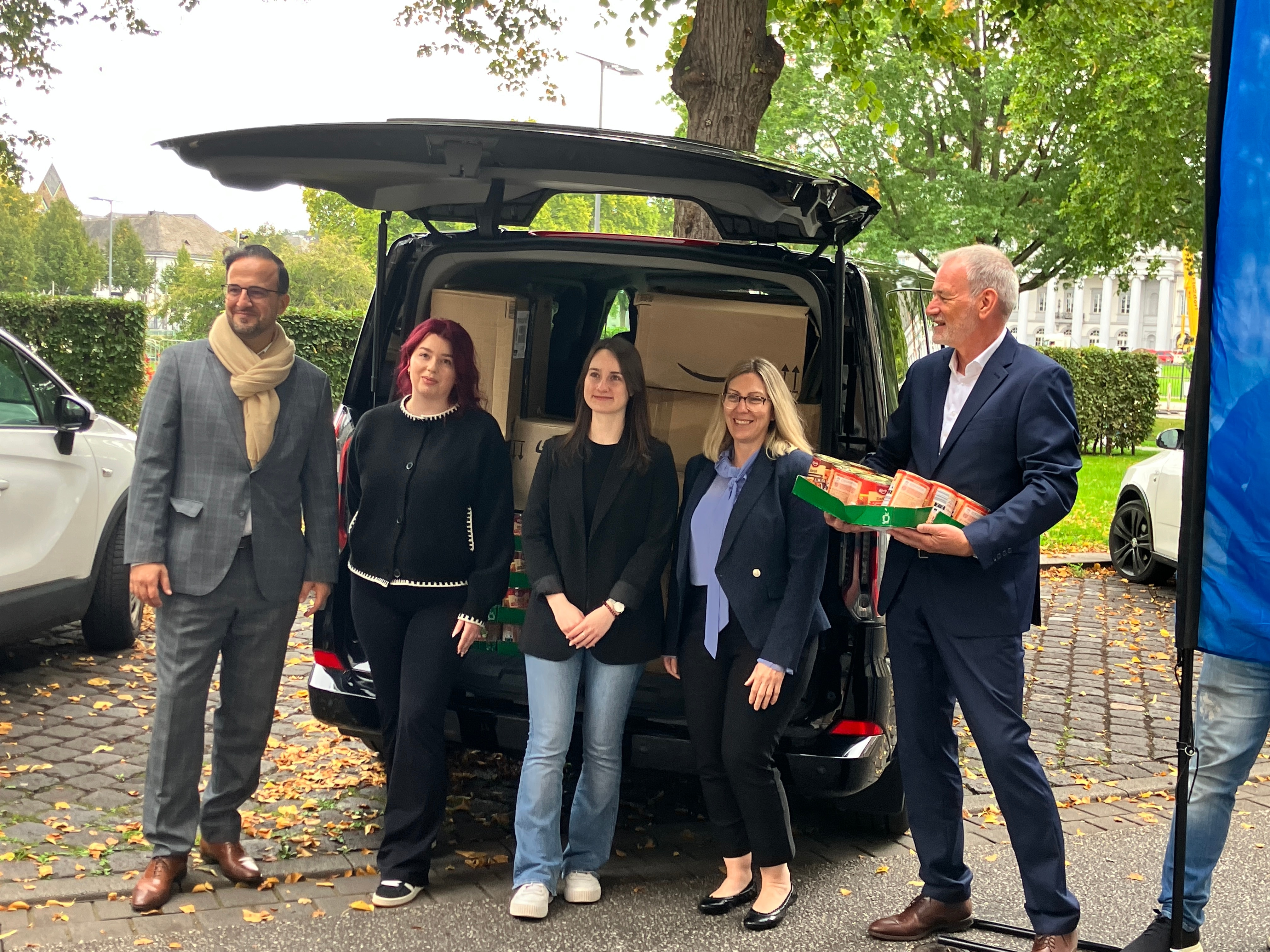 Five people pose for a photo in front of the open back of a van packed with food donations