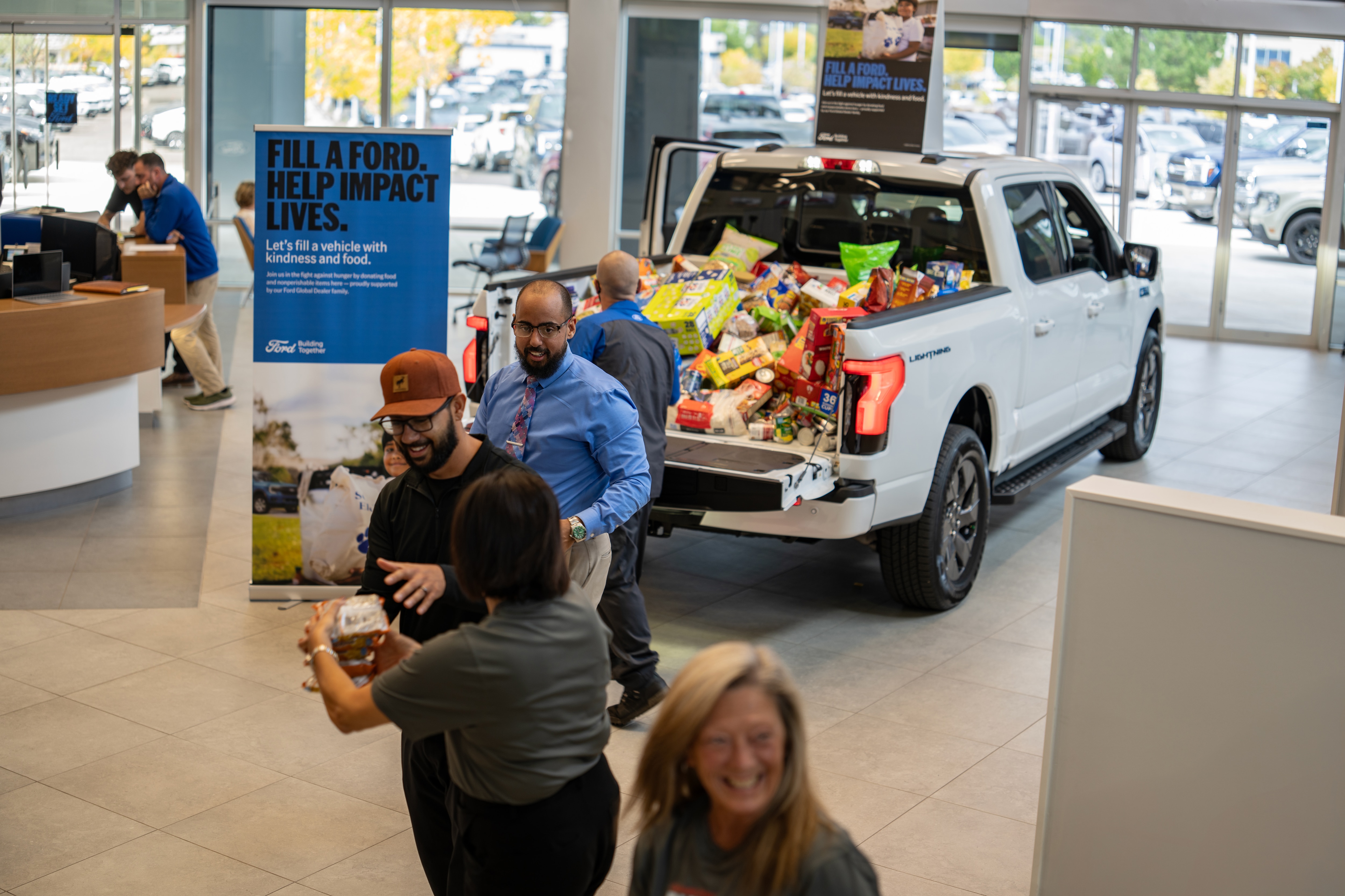 A line of people pass food donation items from person to person until they place them into the back of a truck inside a Ford dealership