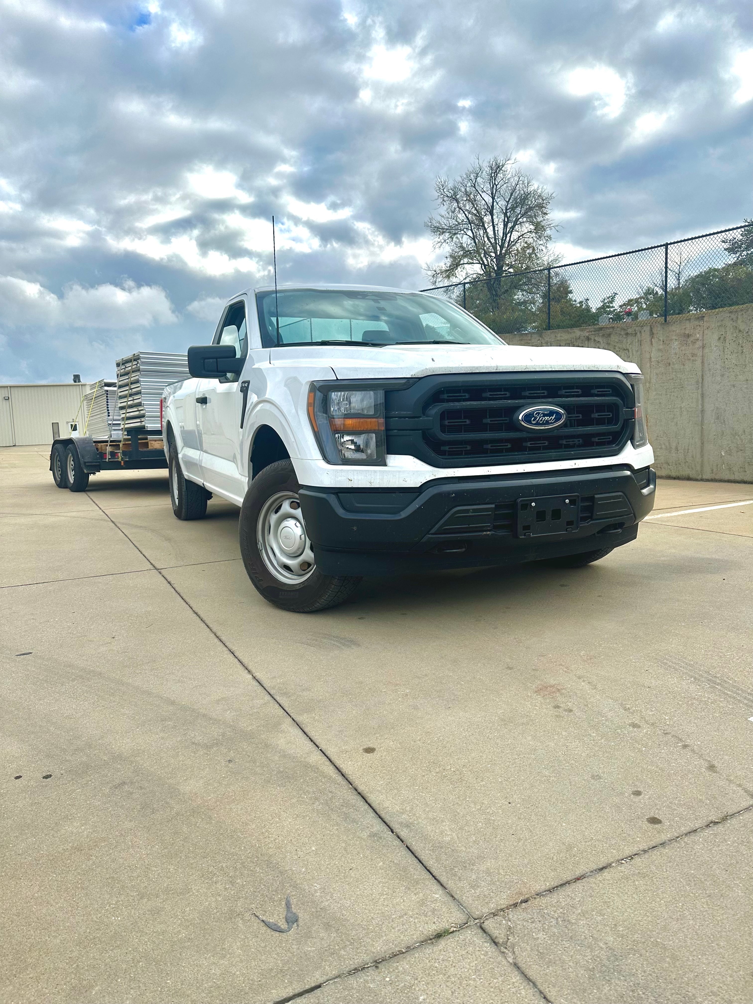 A white truck hauls a trailer with aluminum panels stacked on it