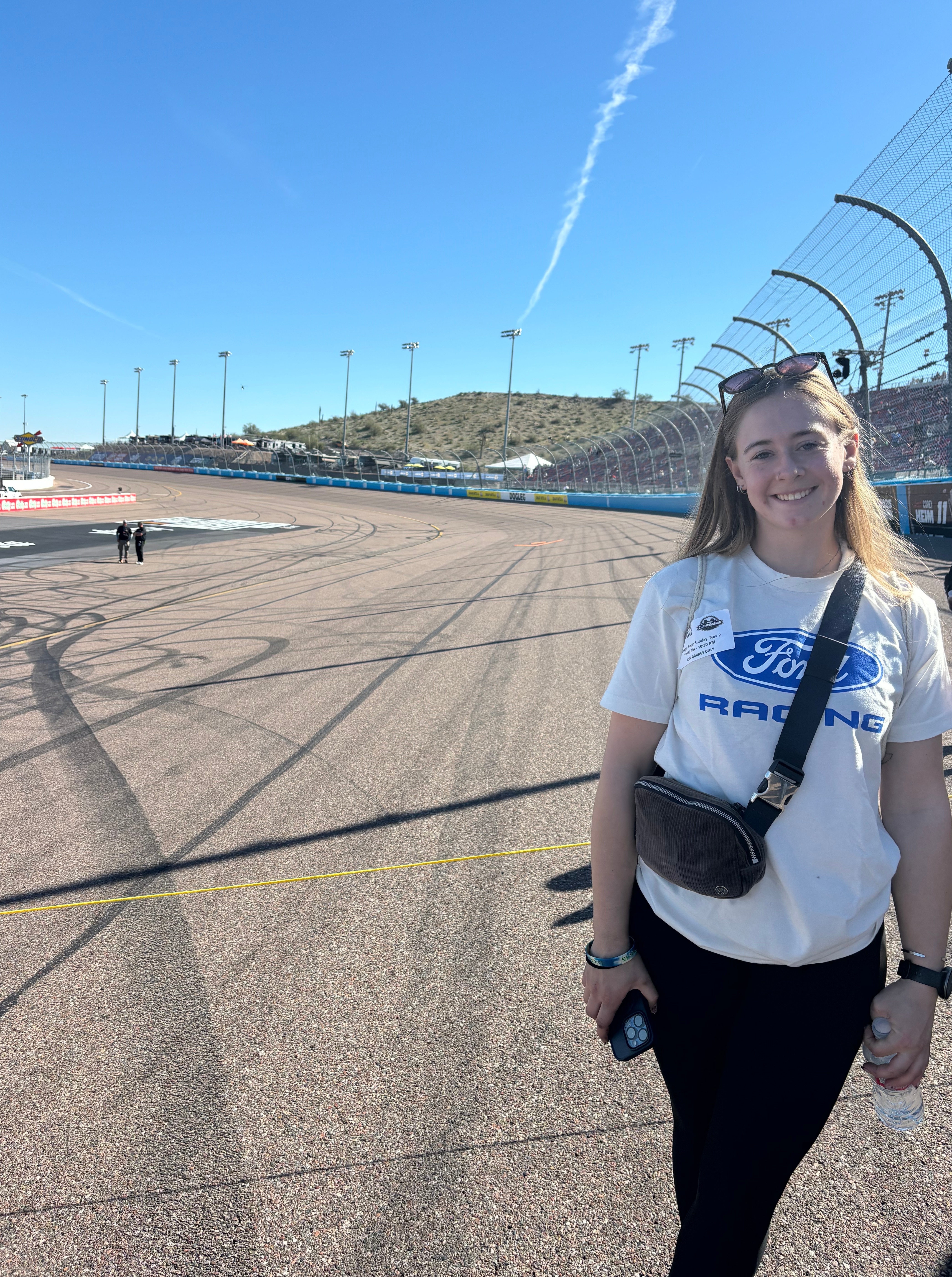 A woman in a white Ford Racing shirt poses on a race track.
