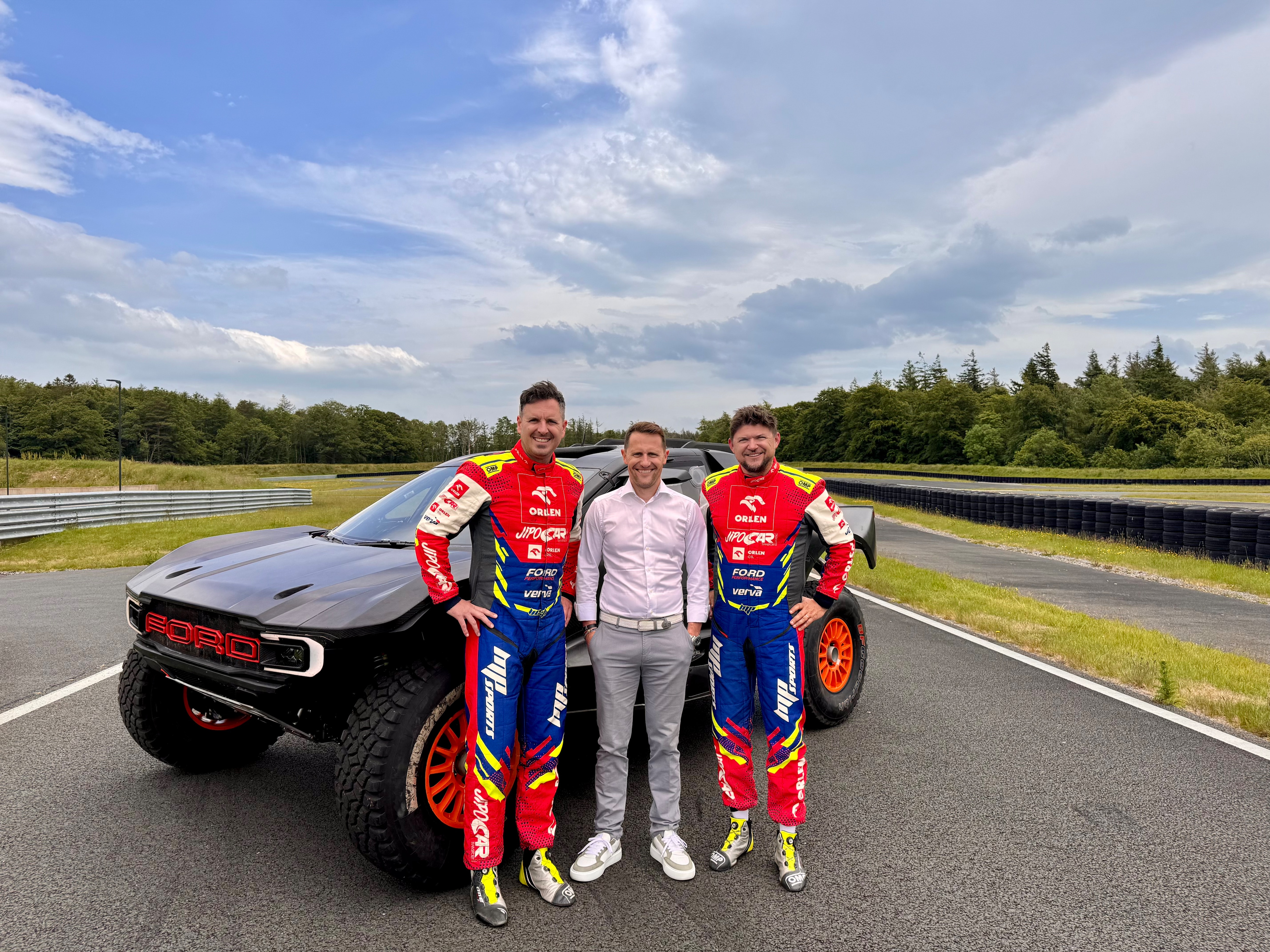 Viktor Chytka (left), Matthew Wilson (center), and Martin Prokop (right) on the grounds of M-Sport with their Ford Raptor T1+.