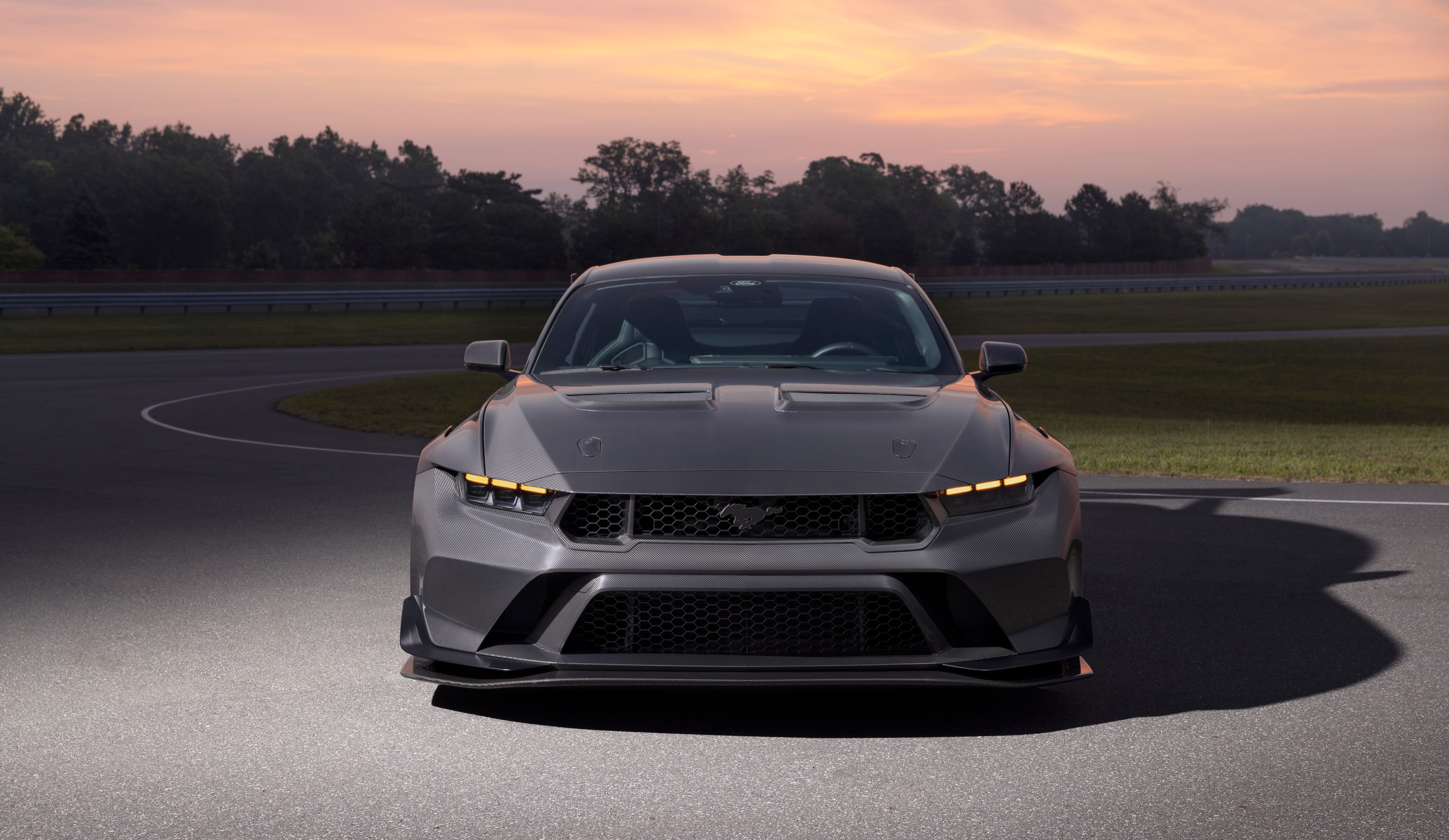New Mustang Liquid Carbon with sleek grey exterior in front of a pink and yellow sunset backdrop.