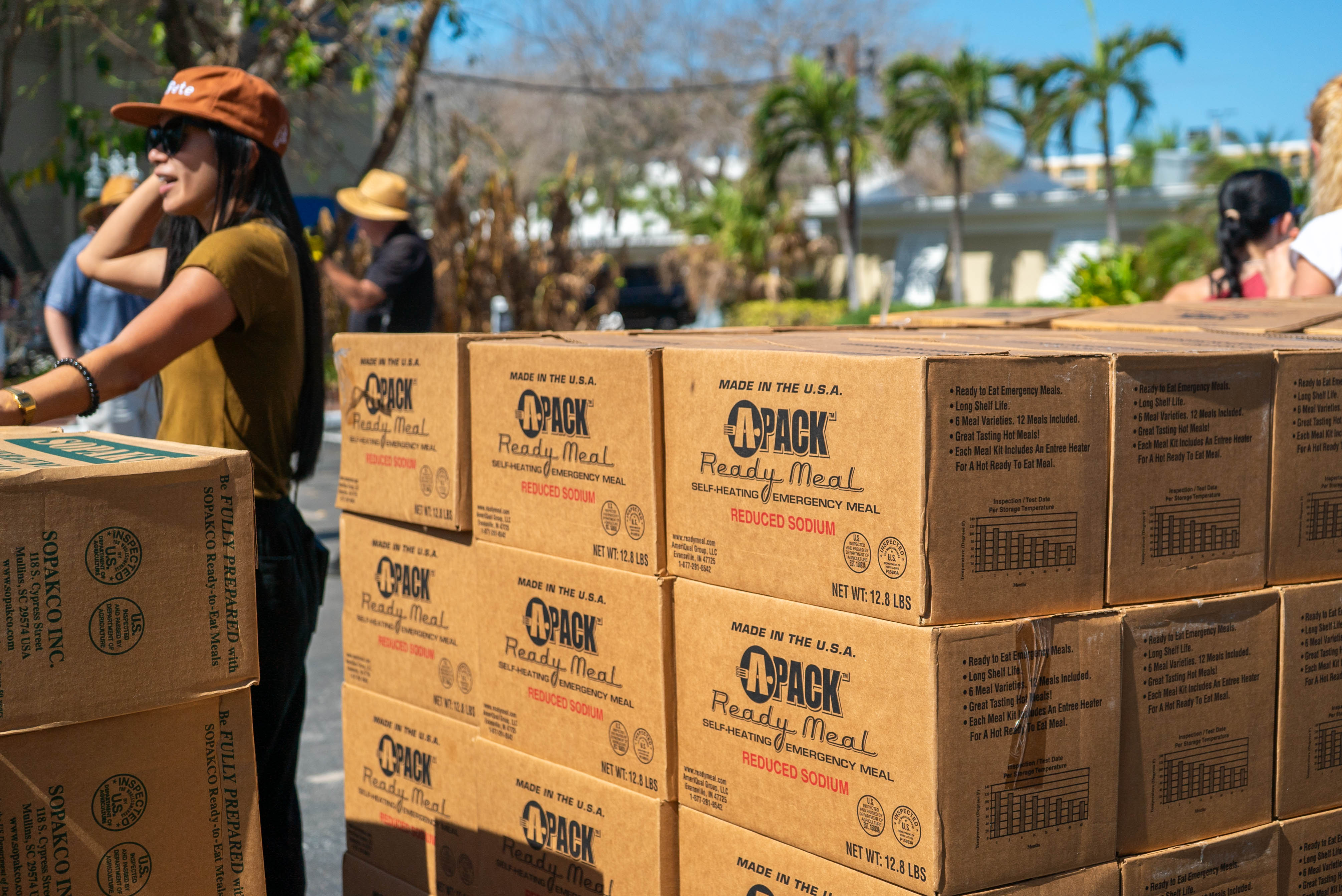 A group of stacked boxes in the foreground with volunteers working in the background