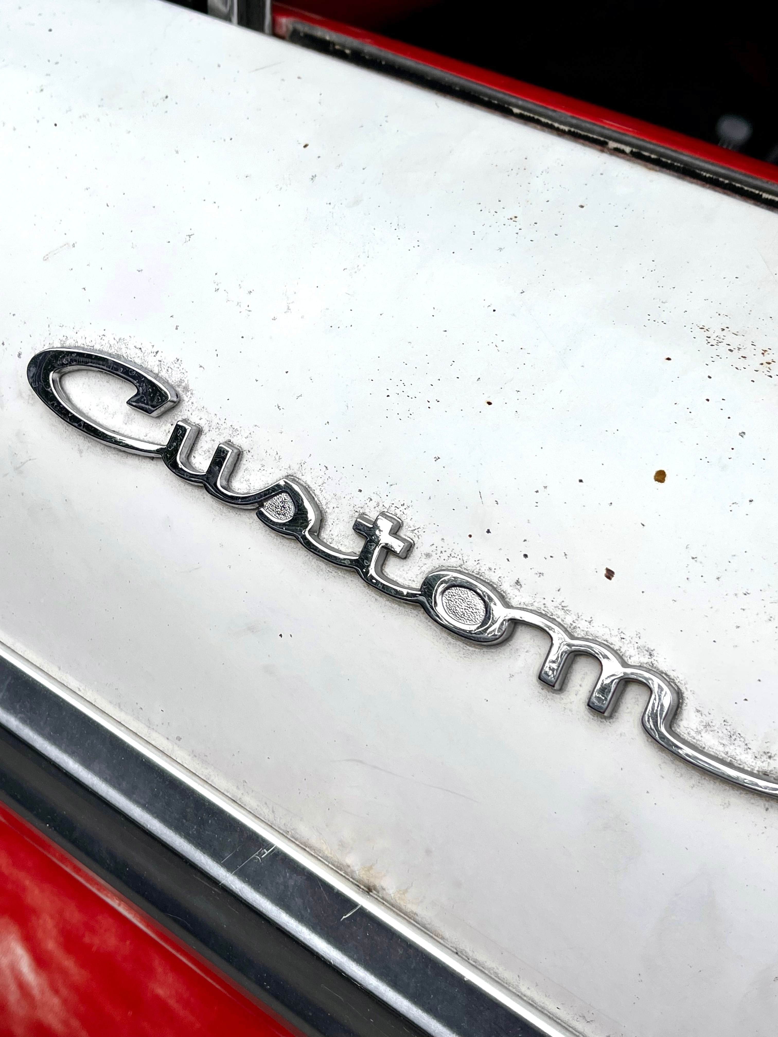 The word "custom" in silver cursive letters on the side of a red 1966 Ford F-250.