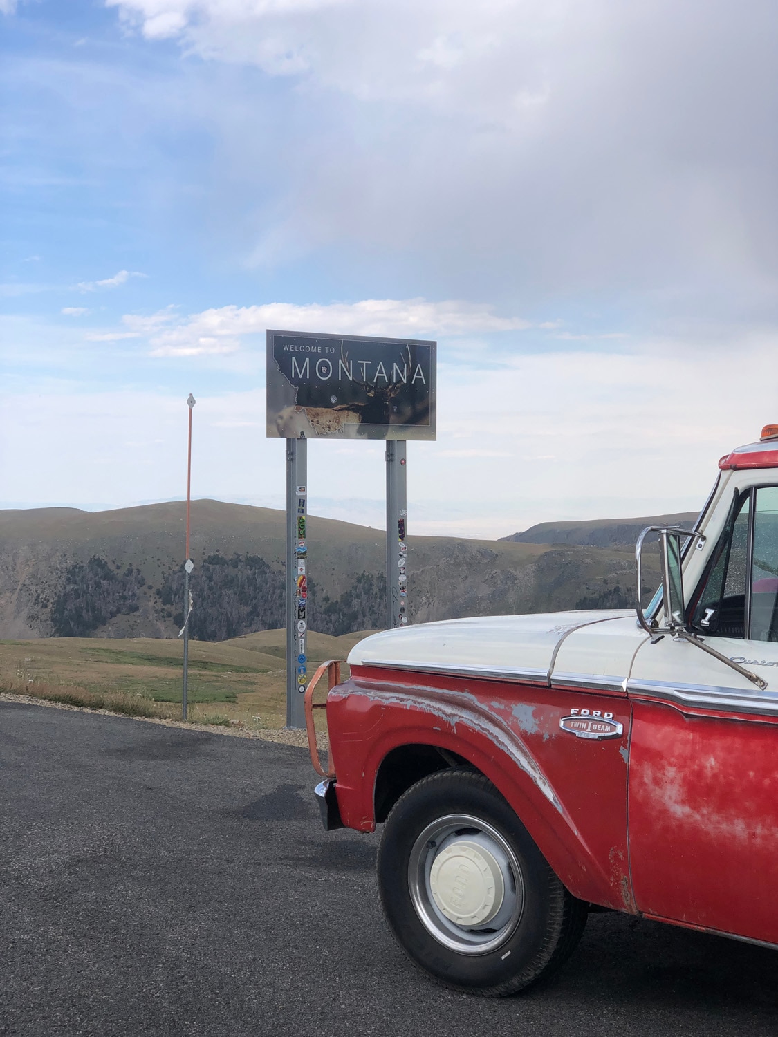 A vintage red truck parked next to a "Welcome to Montana" road sign.