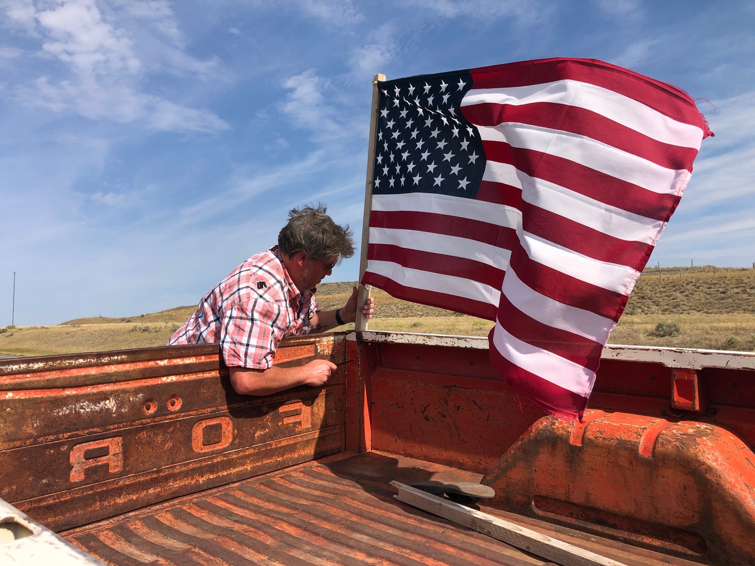  Aman attaches an American Flag to the bed of a vintage Ford pickup truck.