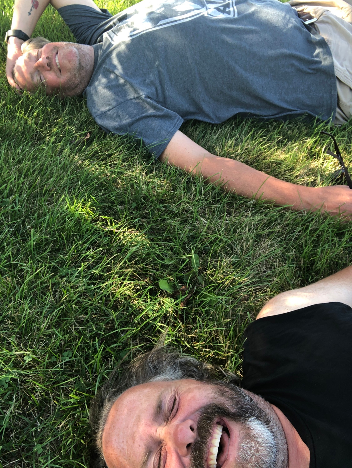 Two men take a selfie while lying in the grass, laughing