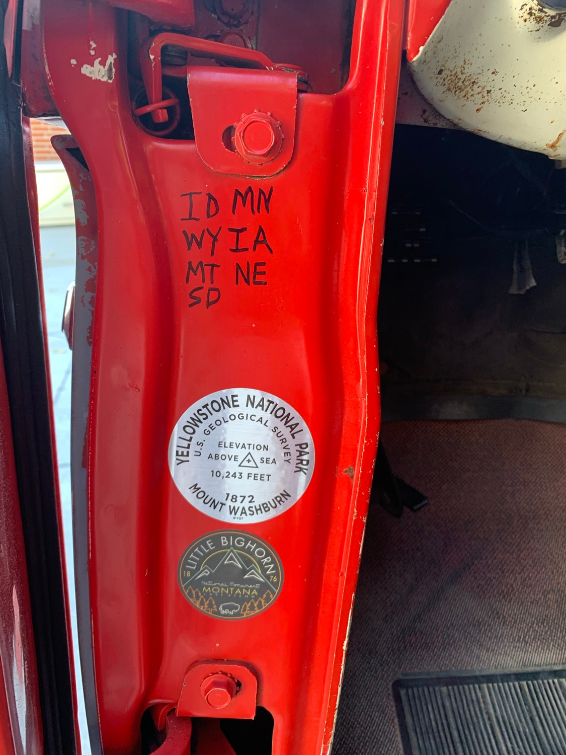 Written in black permanent marker on the inside of a red truck door are the state initials: ID, MN, WY, IA, MT, NE, SD