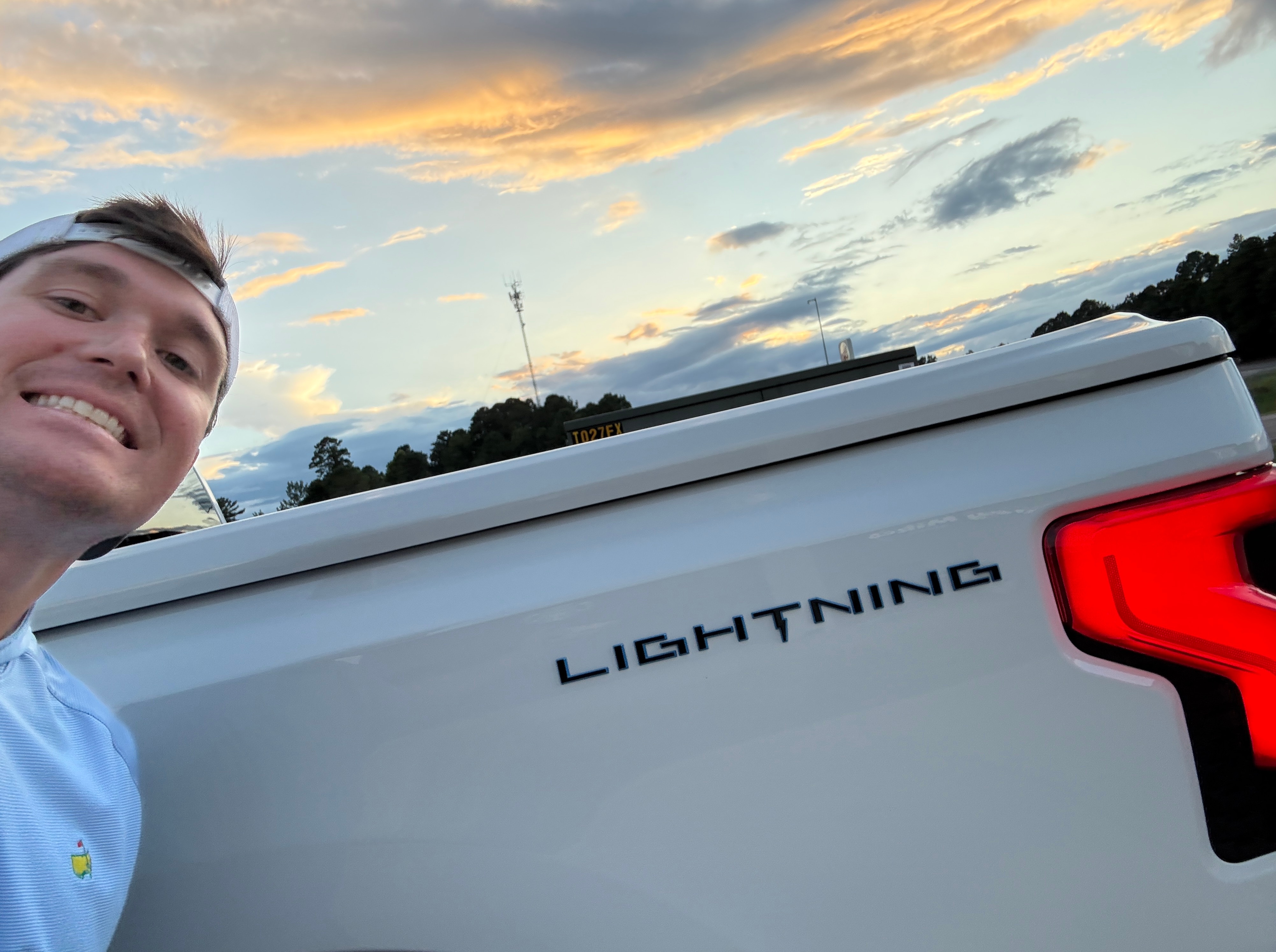 A man grins widely in a selfie with his white Ford F-150 Lightning.