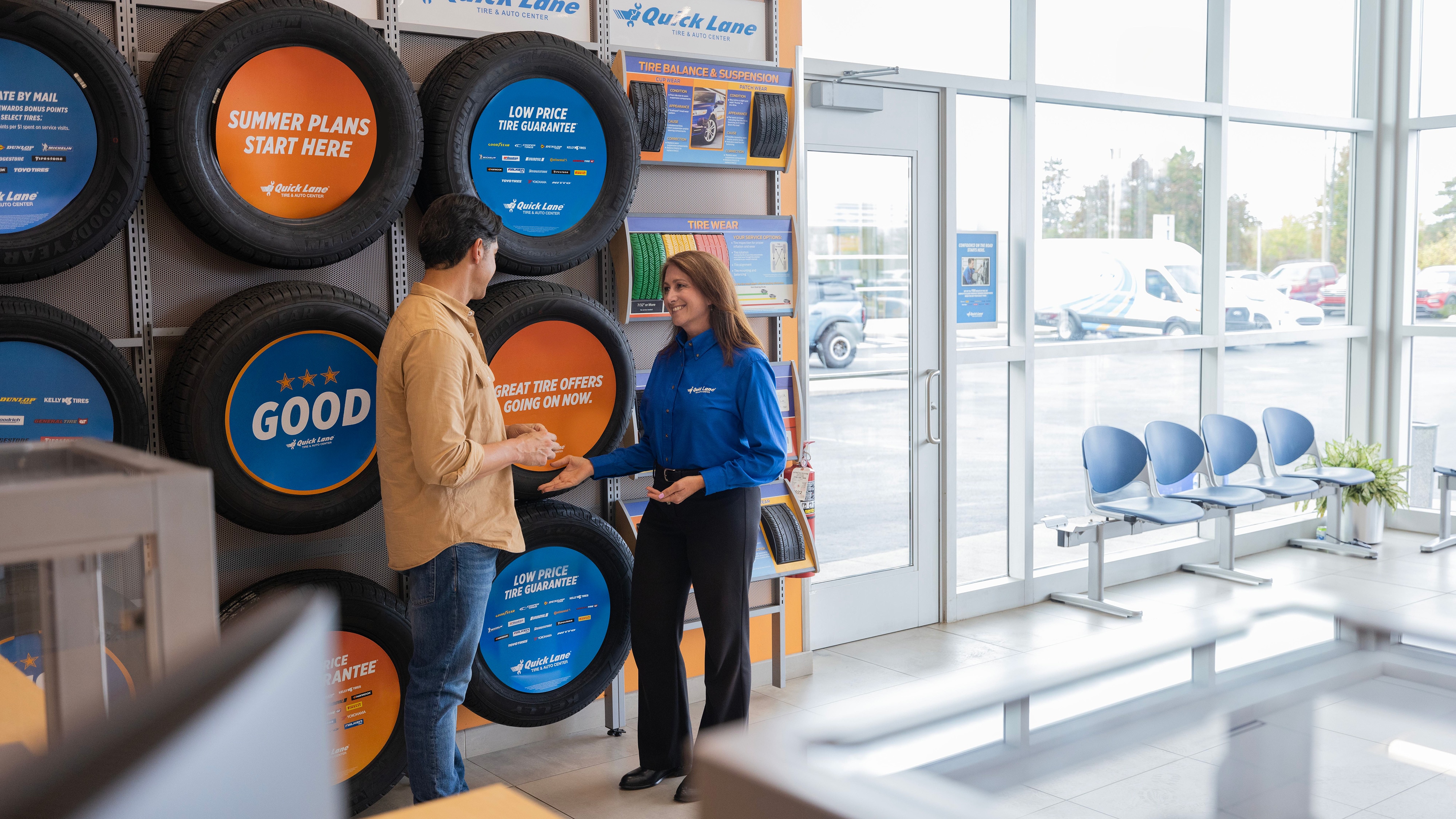 A Quick Lane employee speaks with a customer in front of a tire display.