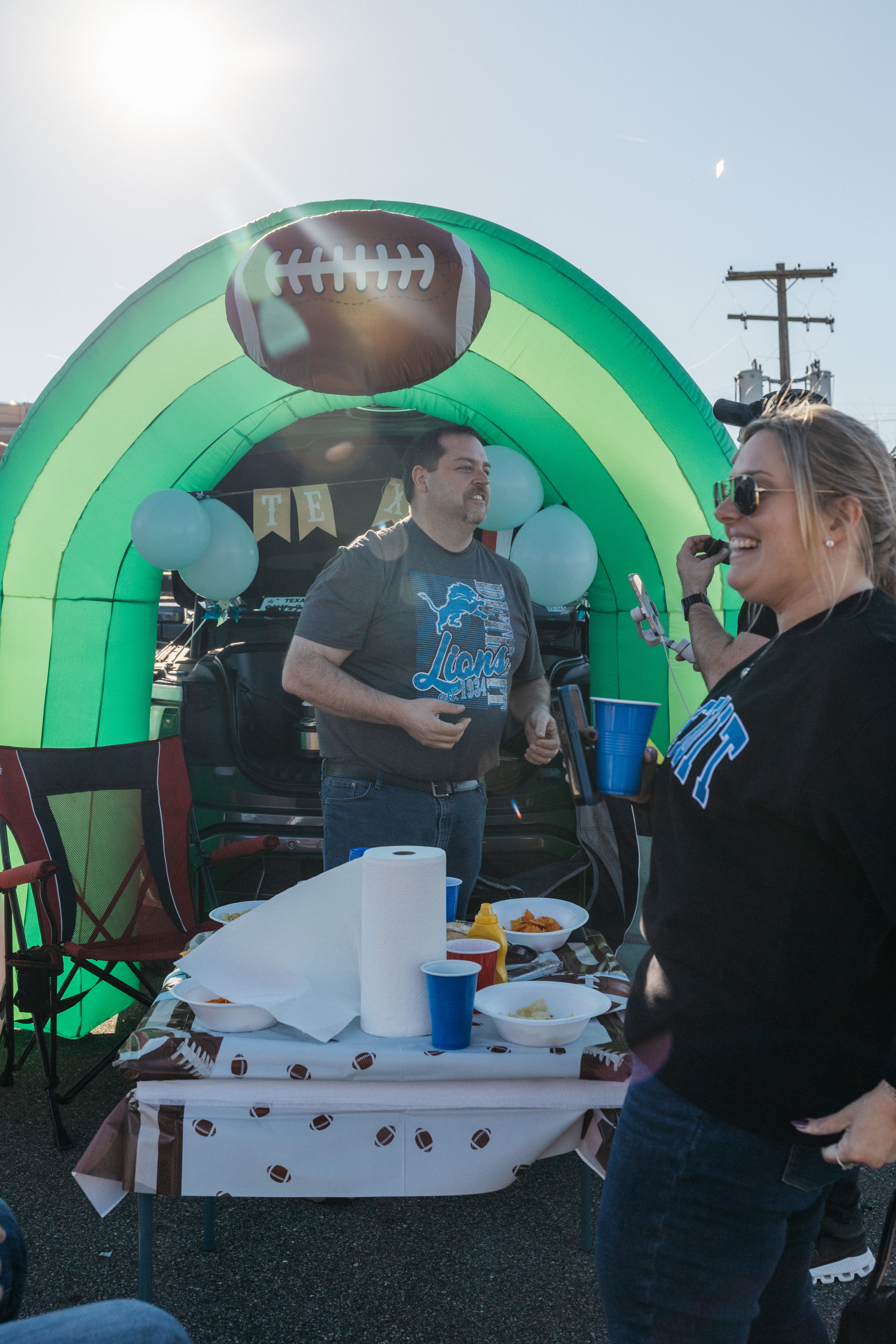 People stand smiling in front of a large inflated decorative arch with a football on it