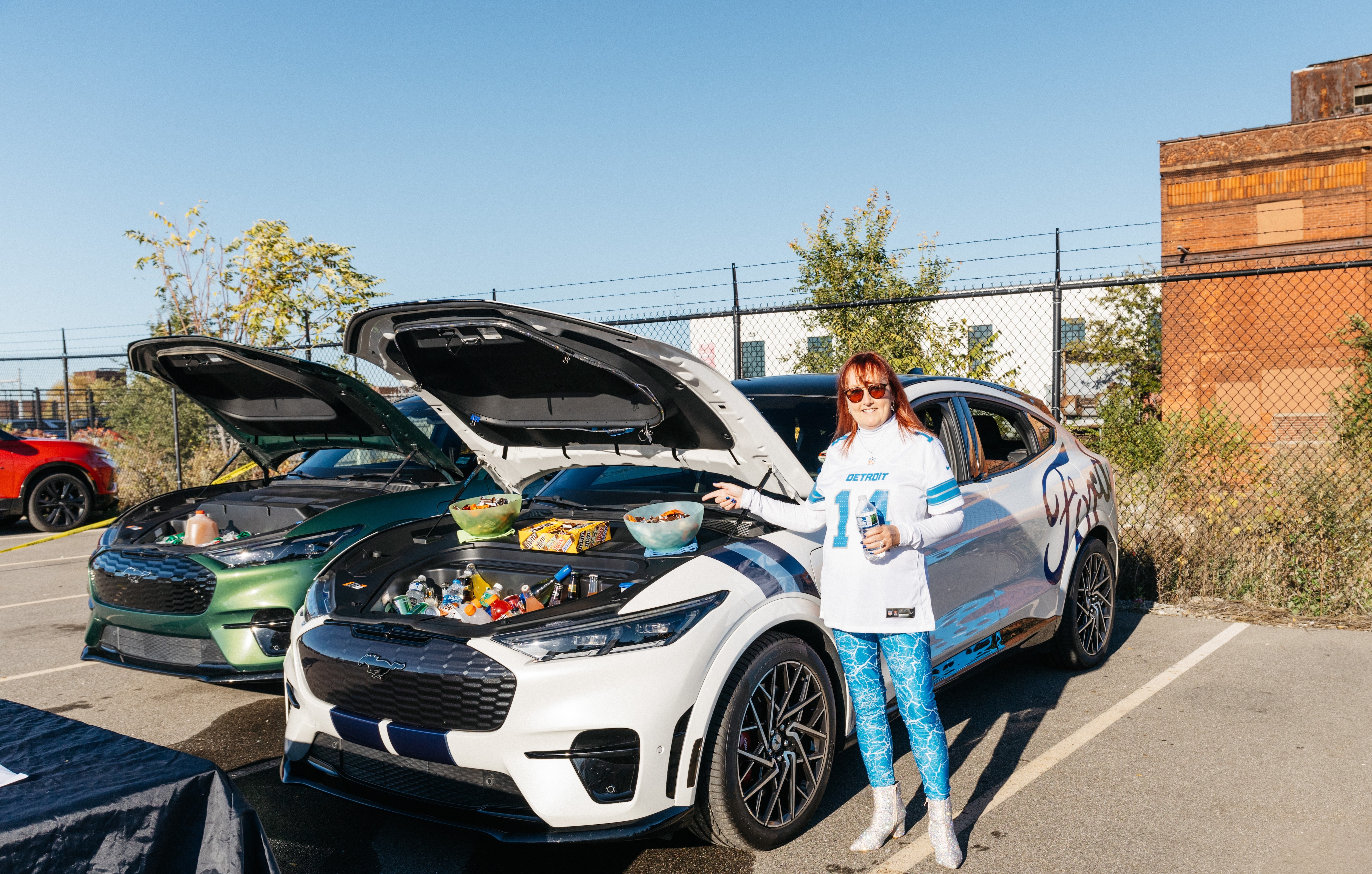 A woman poses next to the open front trunk of her electric vehicle, which is filled with snacks.