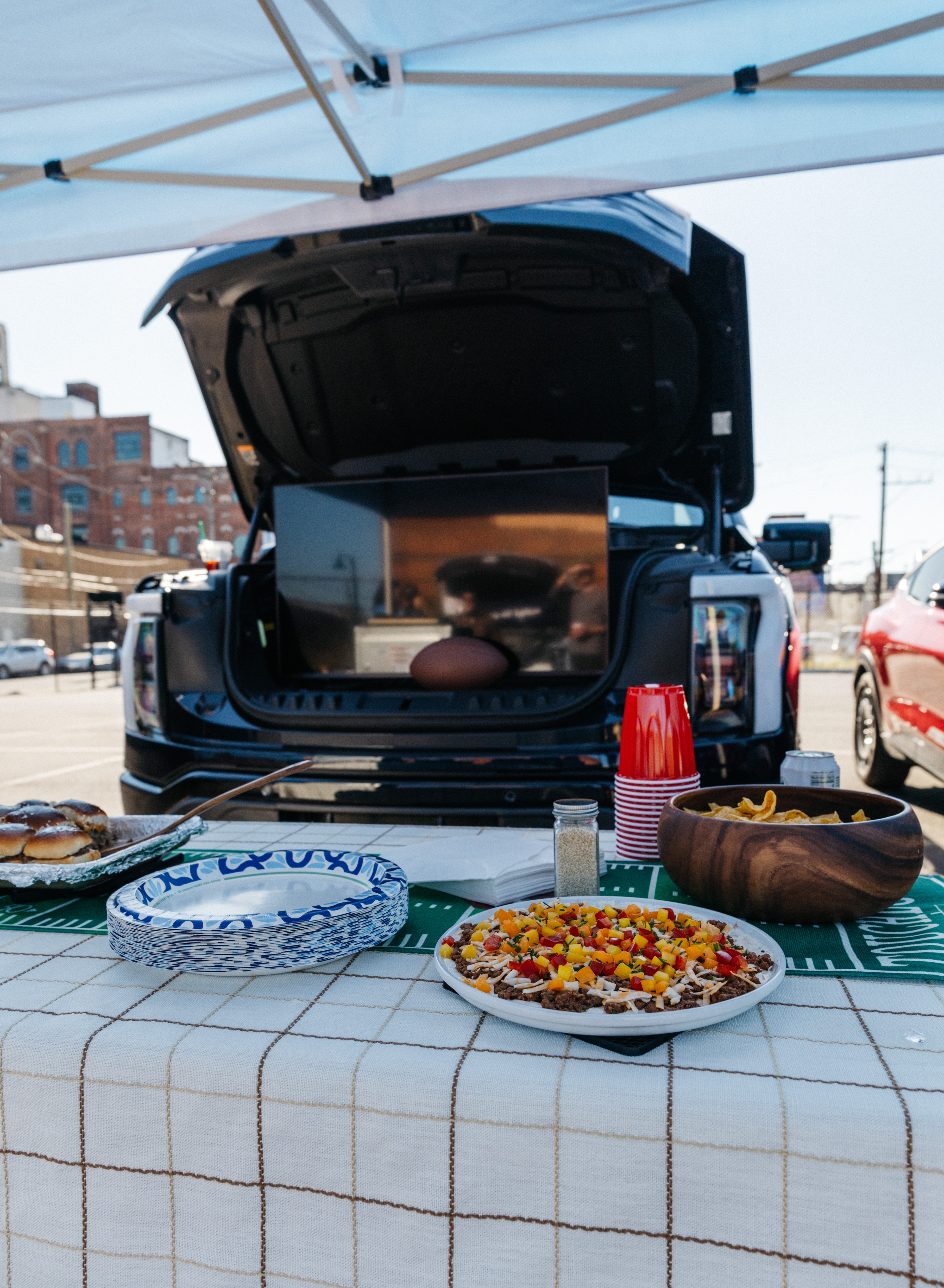 A table with food sits in front of the front trunk of an electric vehicle, which holds a tv