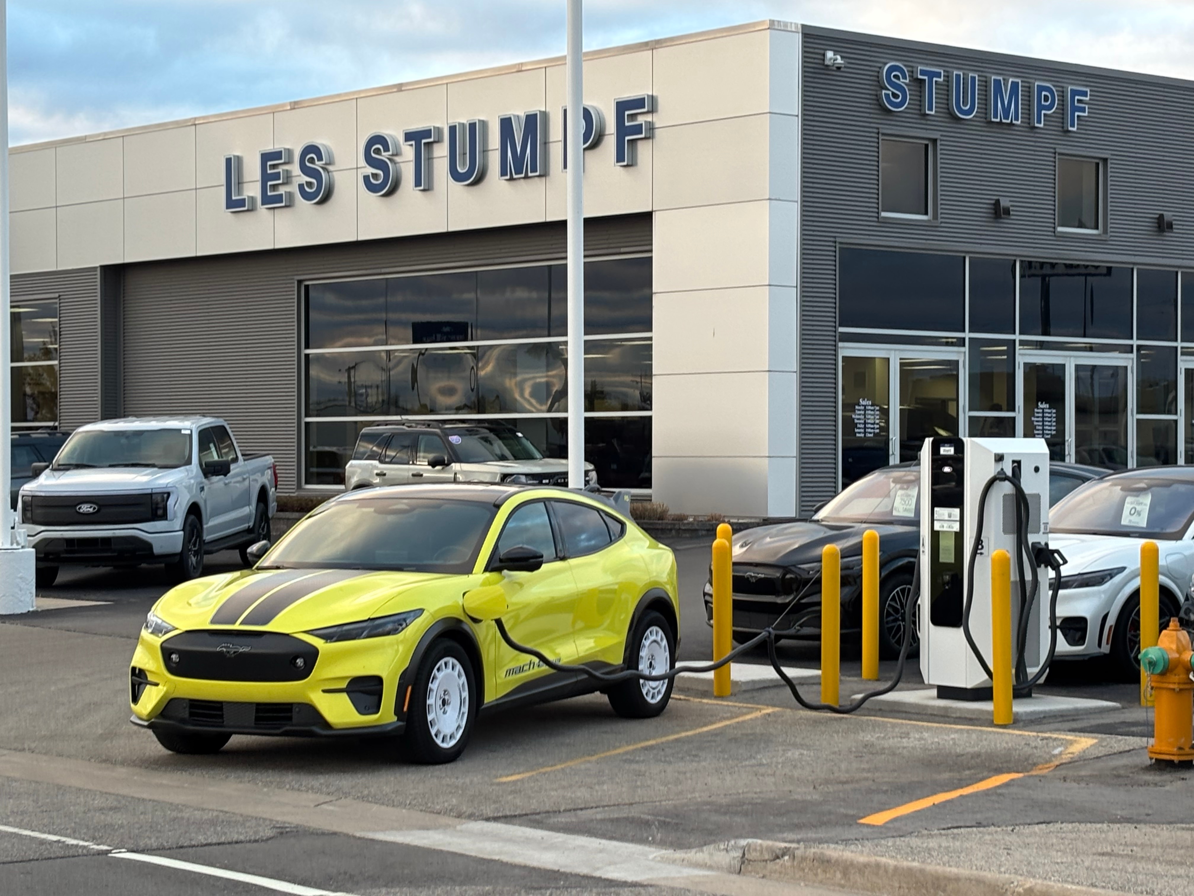 A yellow electric vehicle charges in the parking lot of Les Stumpf Ford.