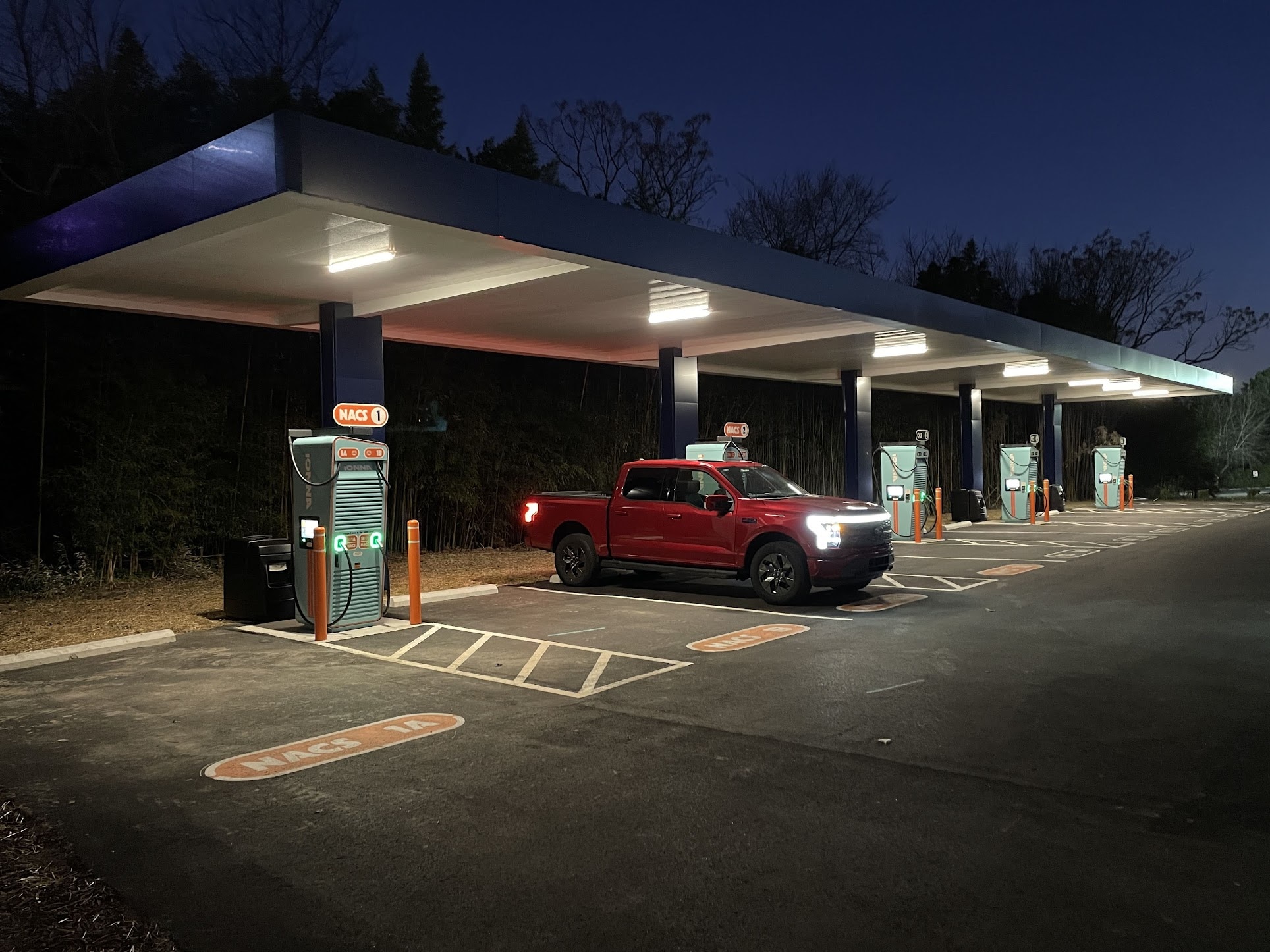 A red F-150 Lightning charging under an awning at night.