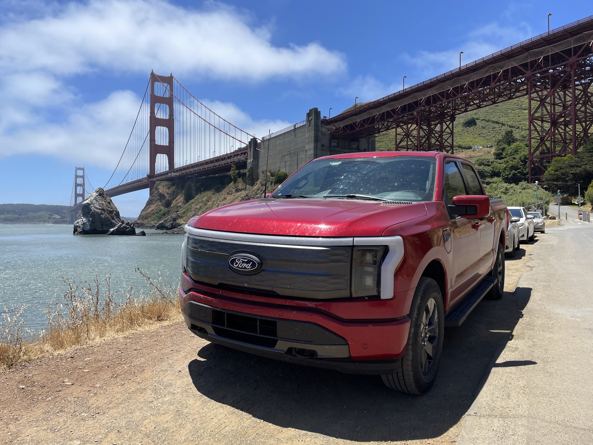 A red Ford F-150 Lightning with the Golden Gate Bridge in the background.
