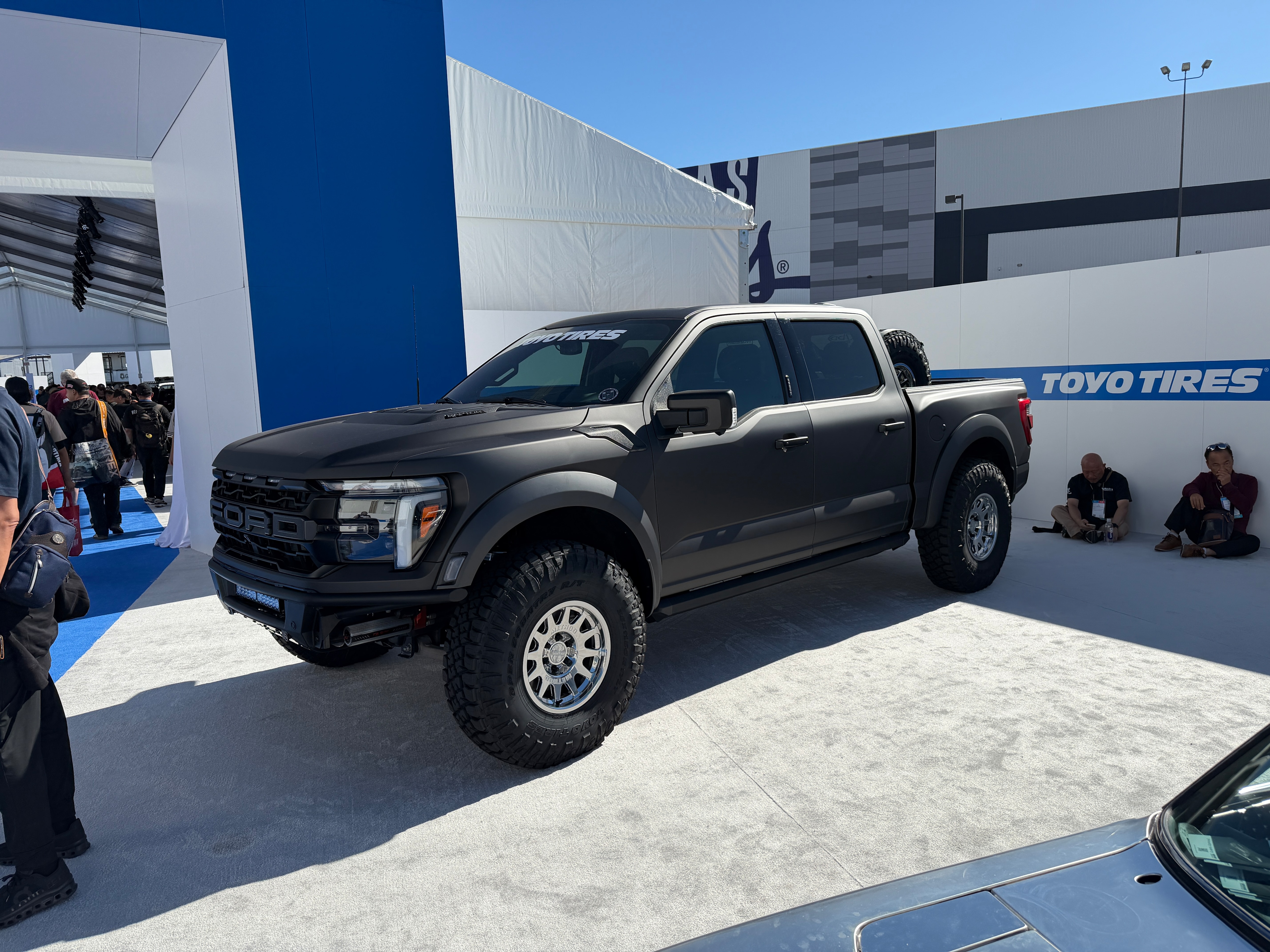 A matte black truck with shiny wheels displayed at a car show