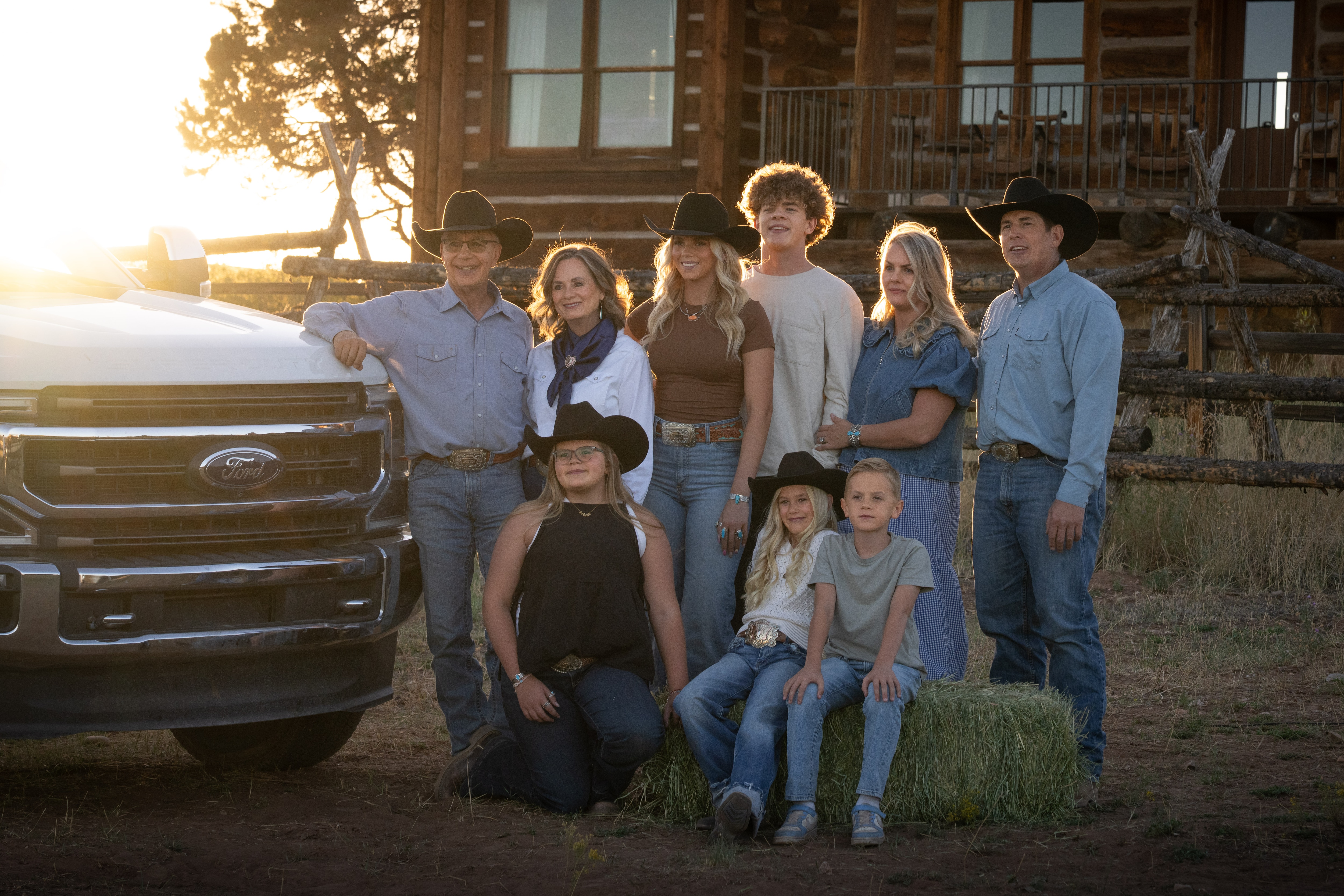 A family poses for a photo with a white Ford truck as the sun sets in the background.
