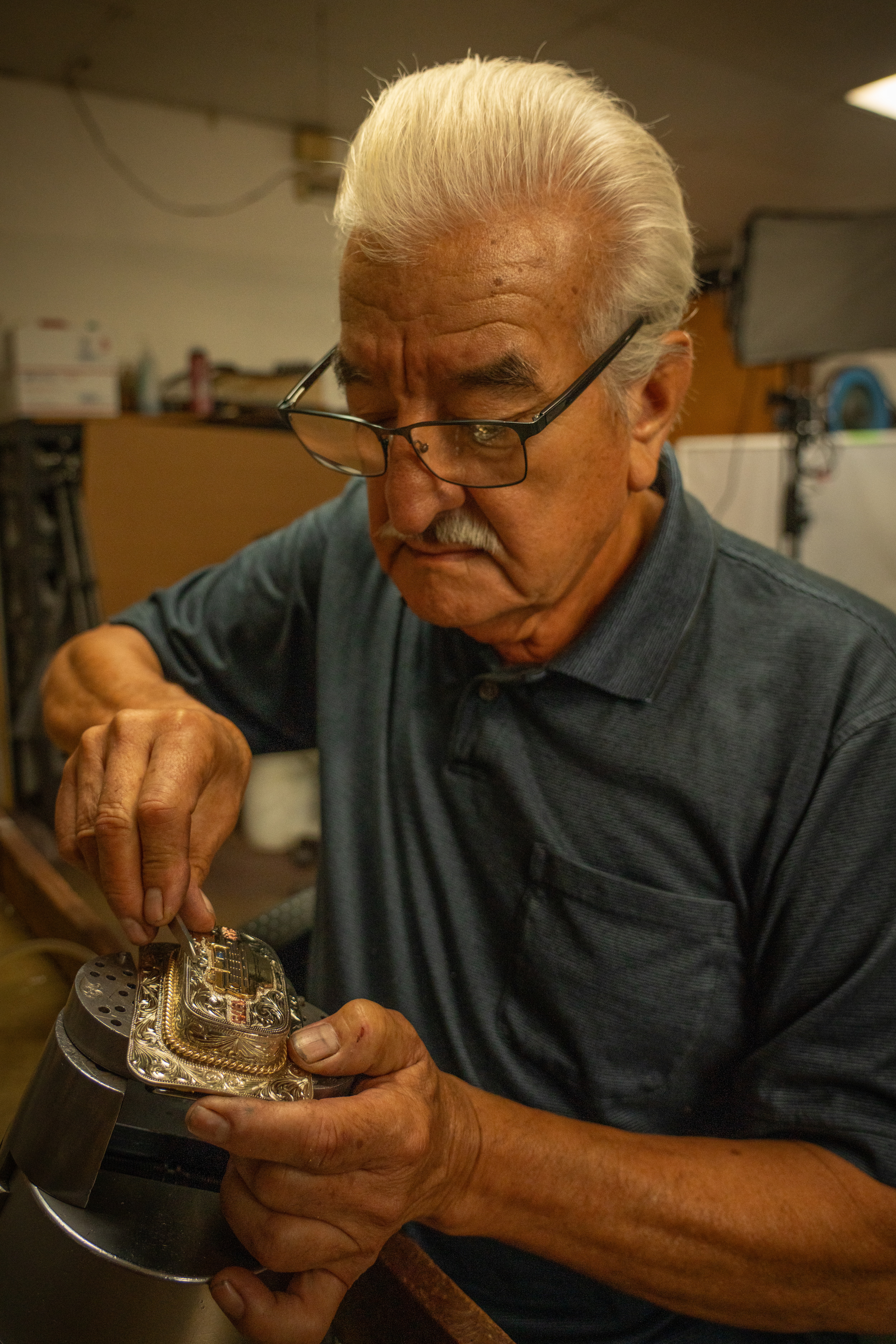 A man focuses intently while crafting a belt buckle. 