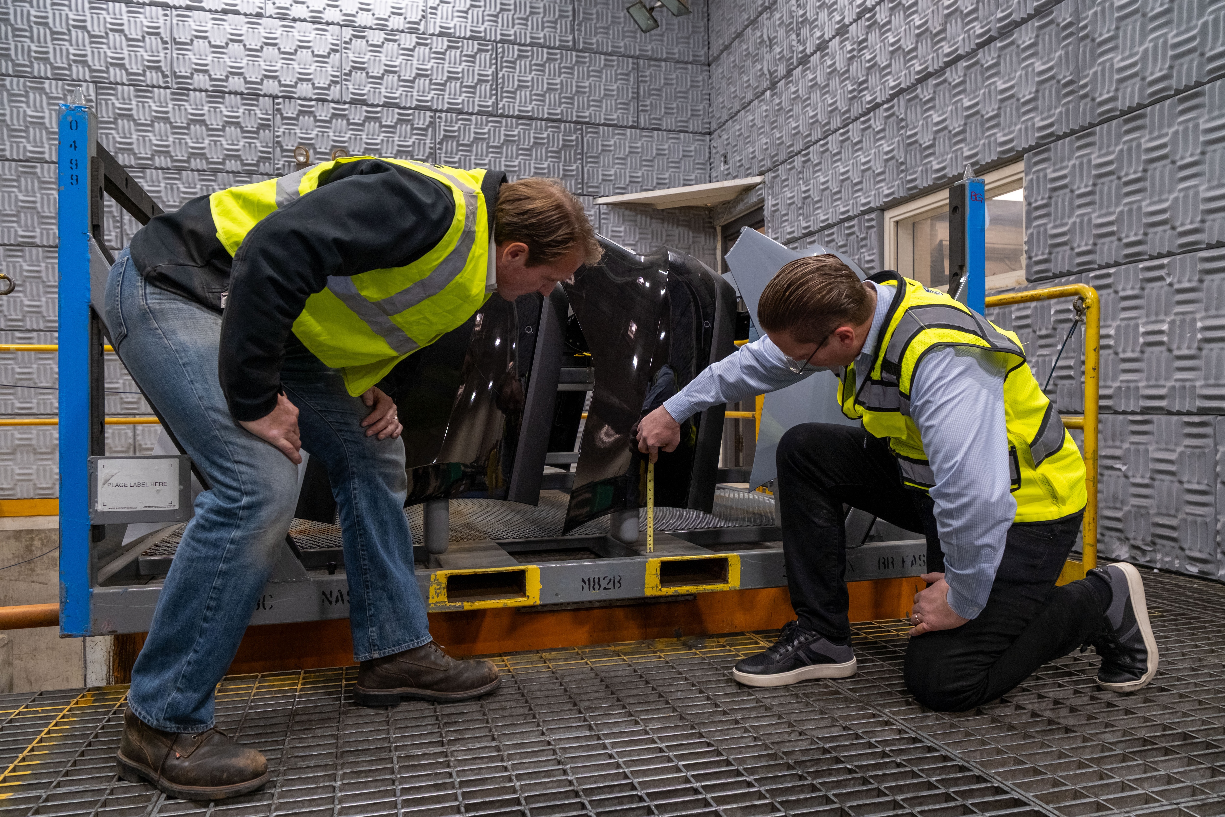 Two men in high-visibility neon yellow vests inspect manufacturing equipment.