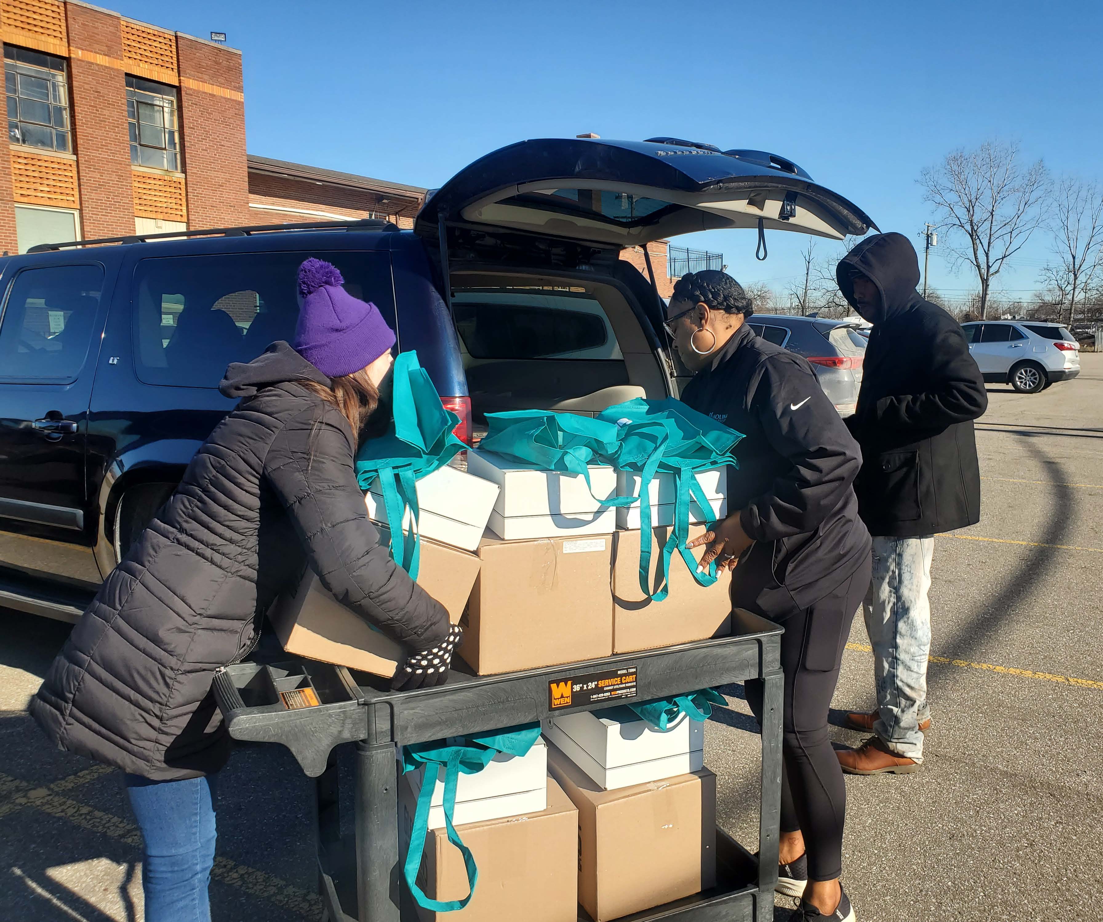 Three volunteers load boxes packed with donations into the back of a vehicle.