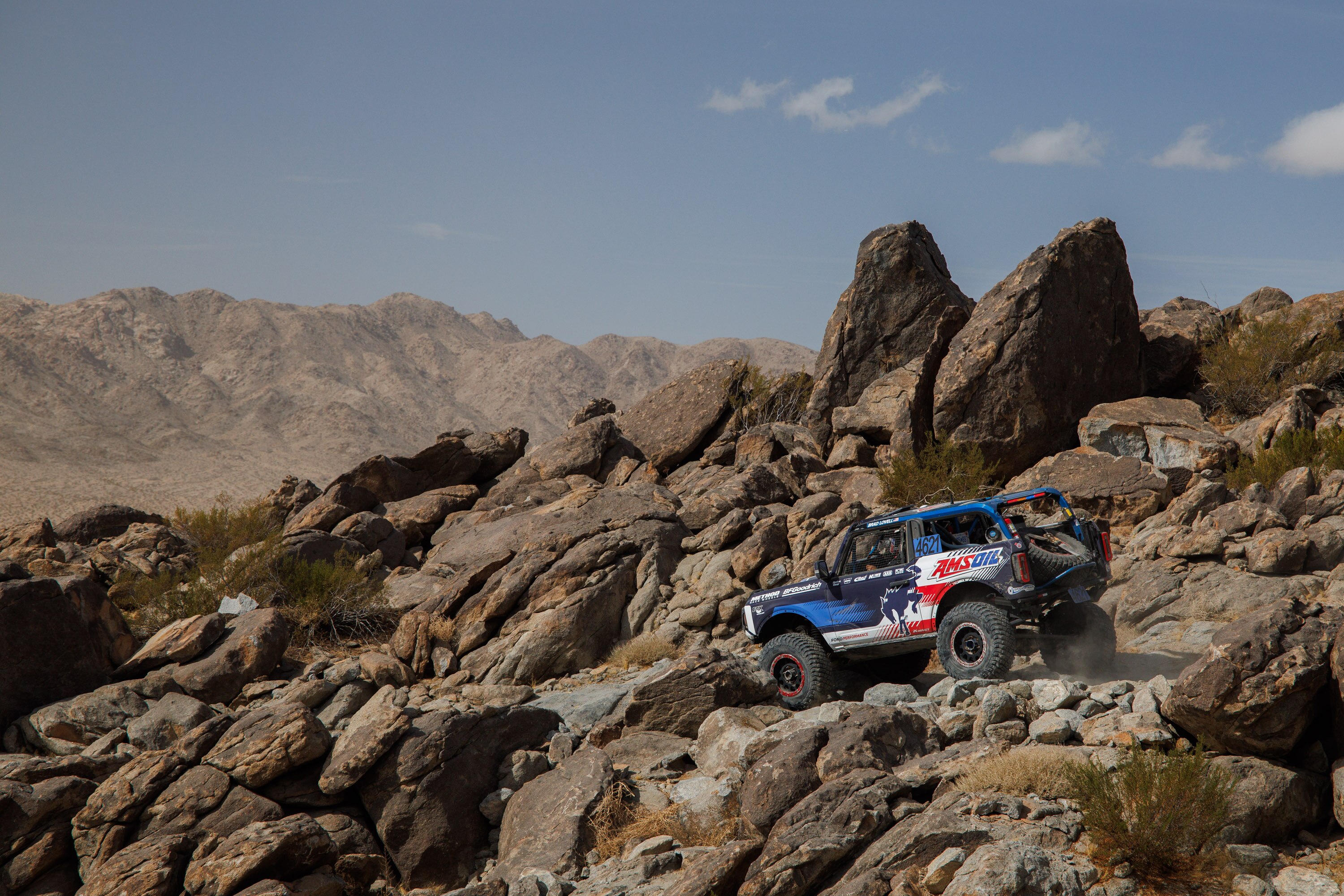 A blue Bronco drives off road on rocky terrain.