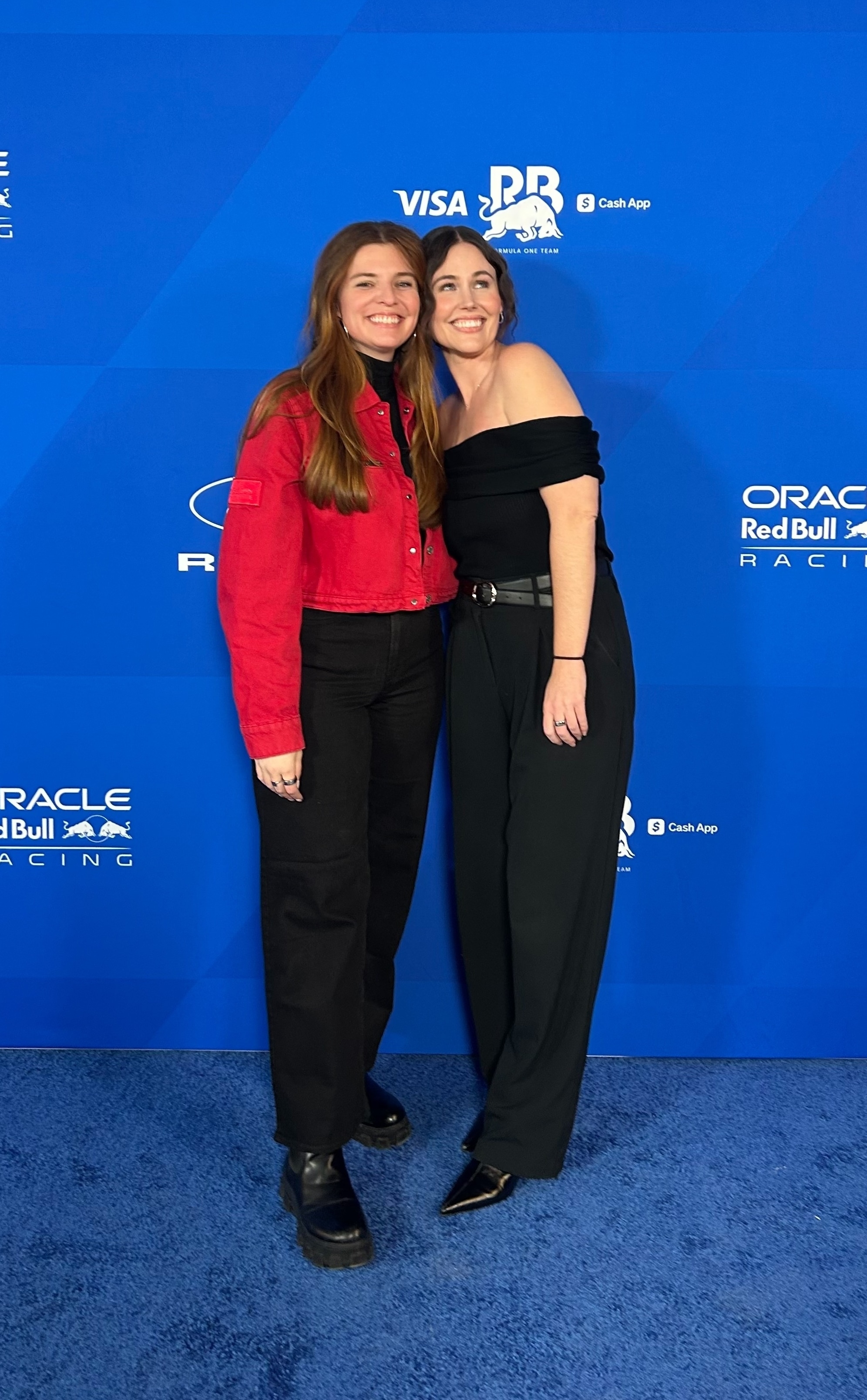 Two women in business attire pose for a photo in front of a blue backdrop.