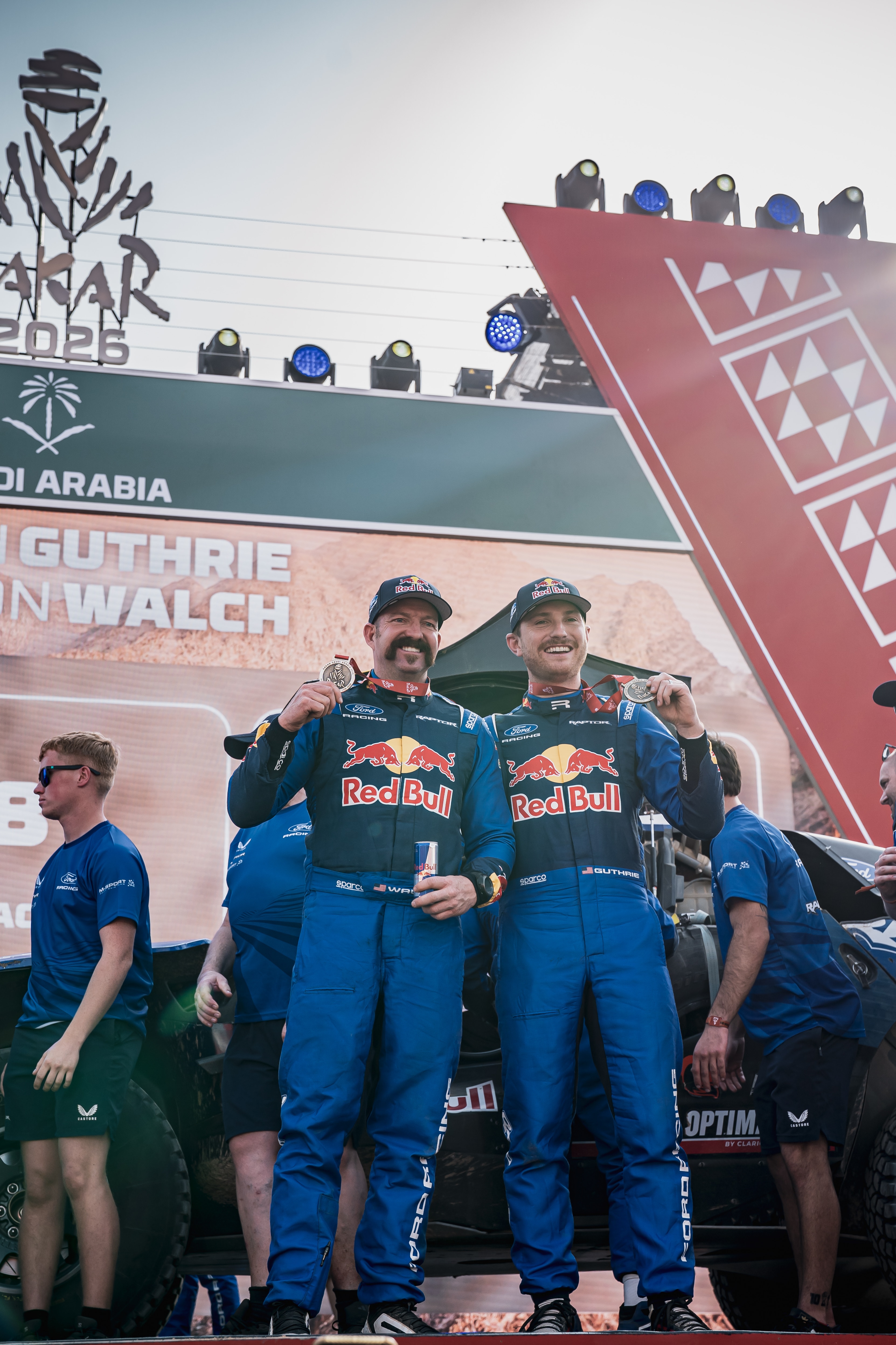 Two men in Ford Red Bull racing uniforms pose with medals on the podium.