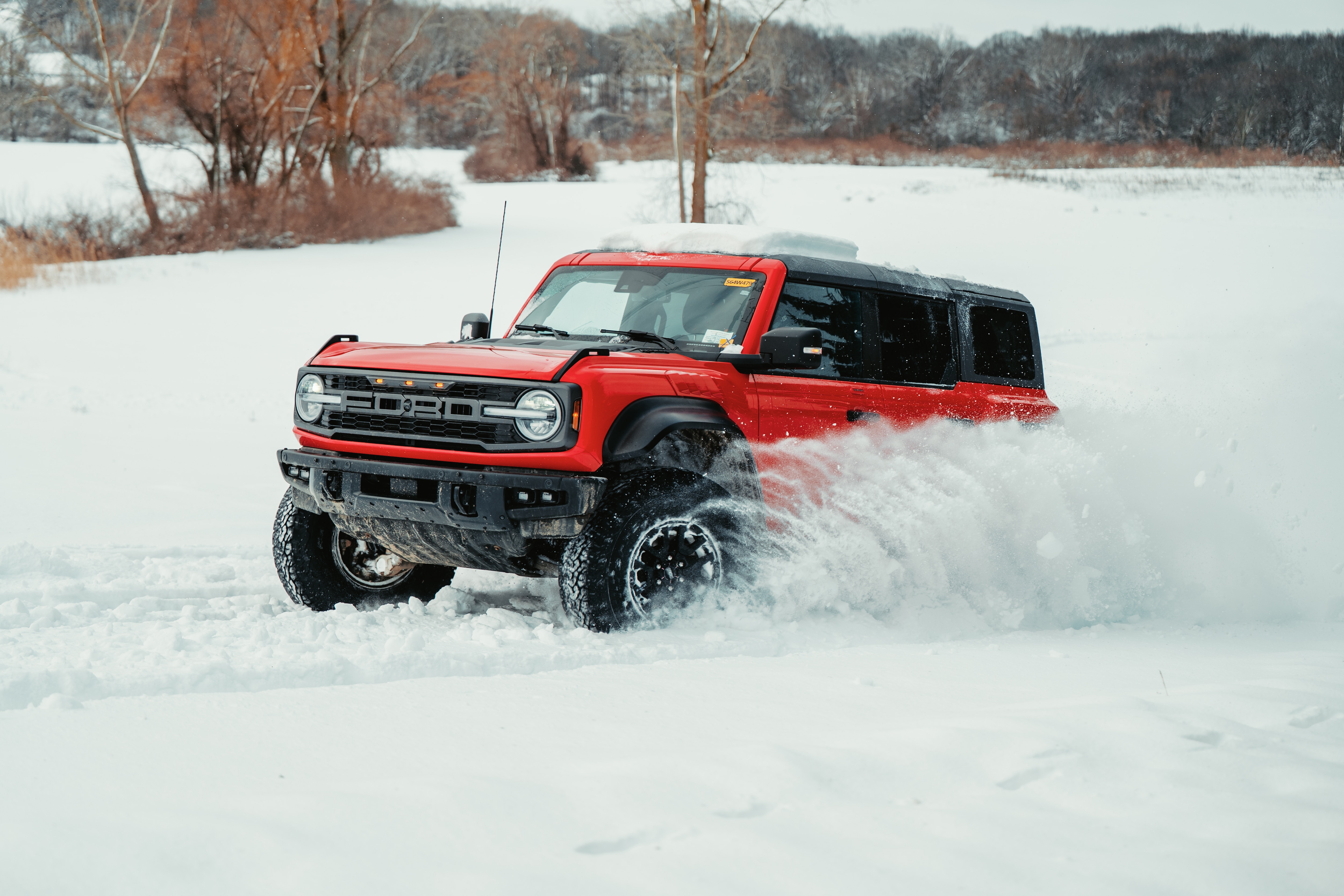 A red Ford Bronco drives through several inches of snow.